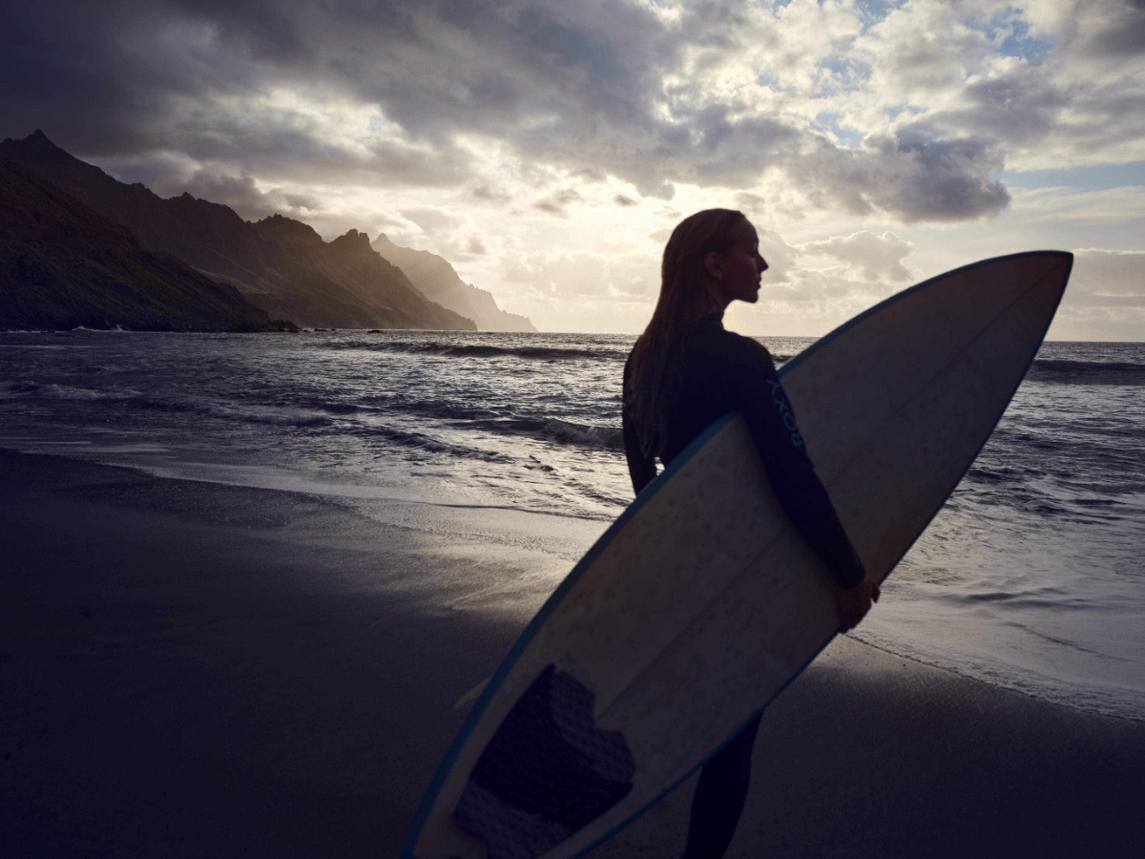 a woman holding a surfboard infront of the ocean