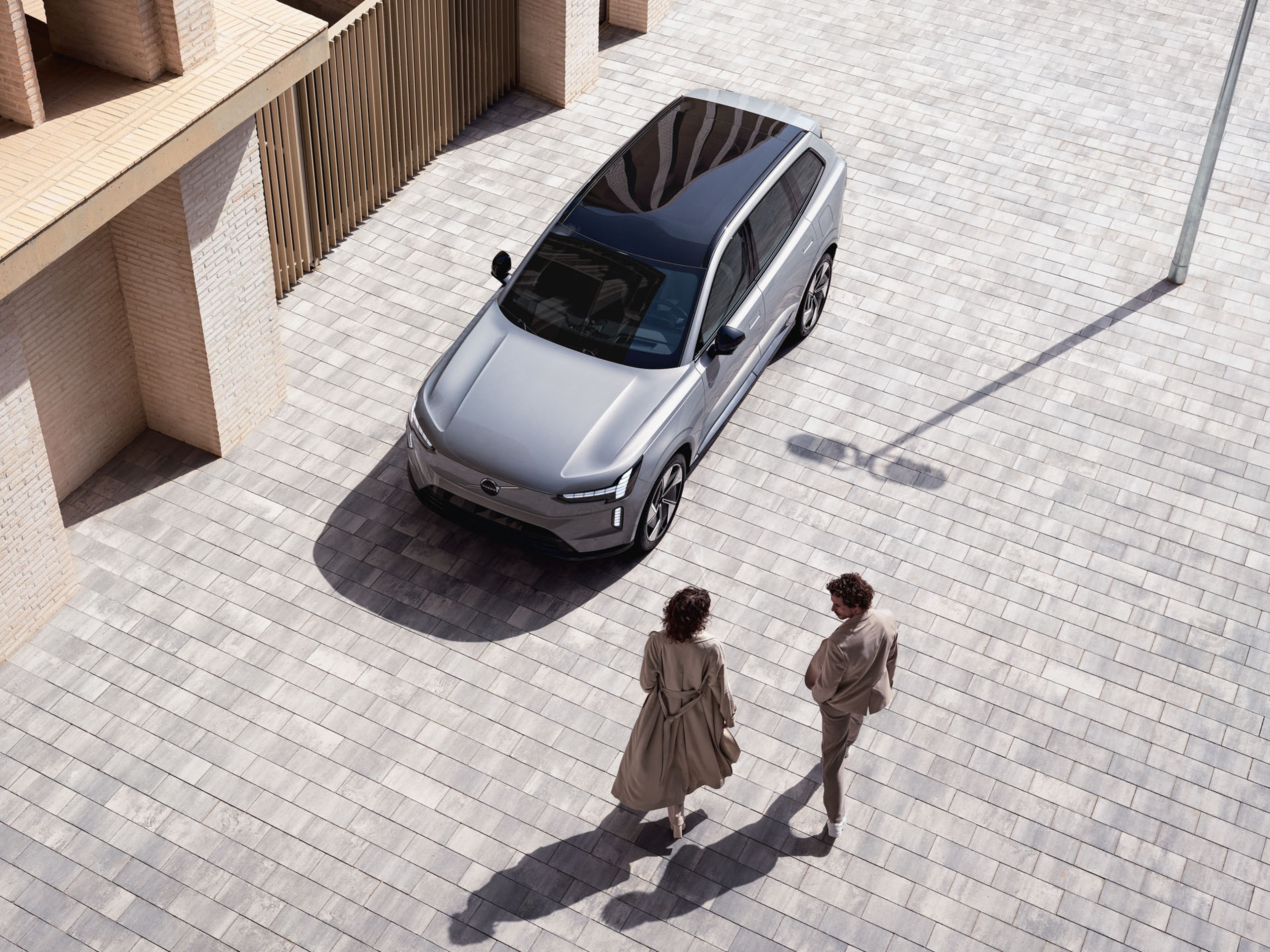 Dos personas caminando junto a un Volvo EX90 en el que destaca su techo solar