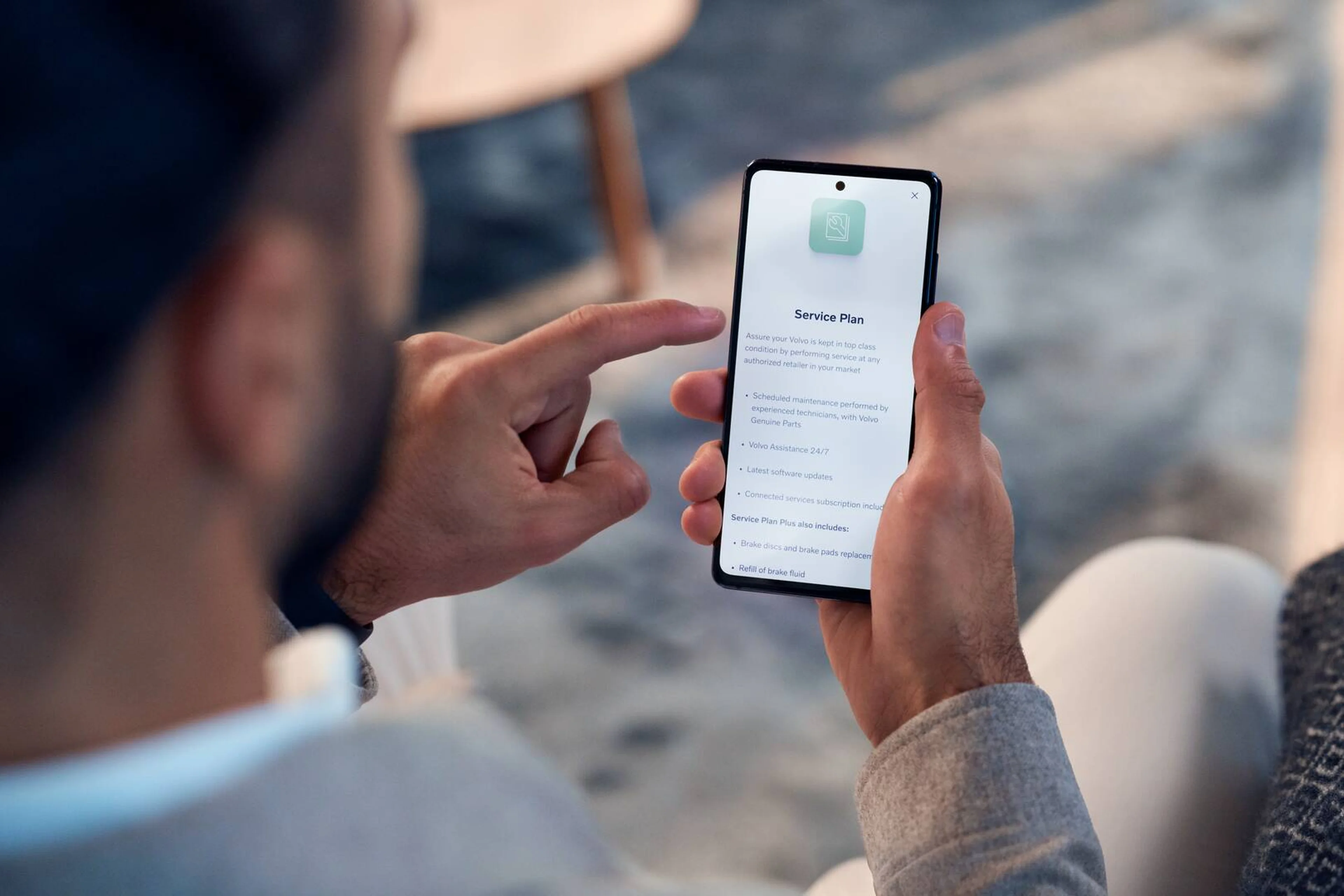 En person holder en smartphone, der viser en "Serviceaftale"-app på skærmen. Stemningen er afslappet og antyder fokus på bilvedligeholdelse eller supporttjenester.