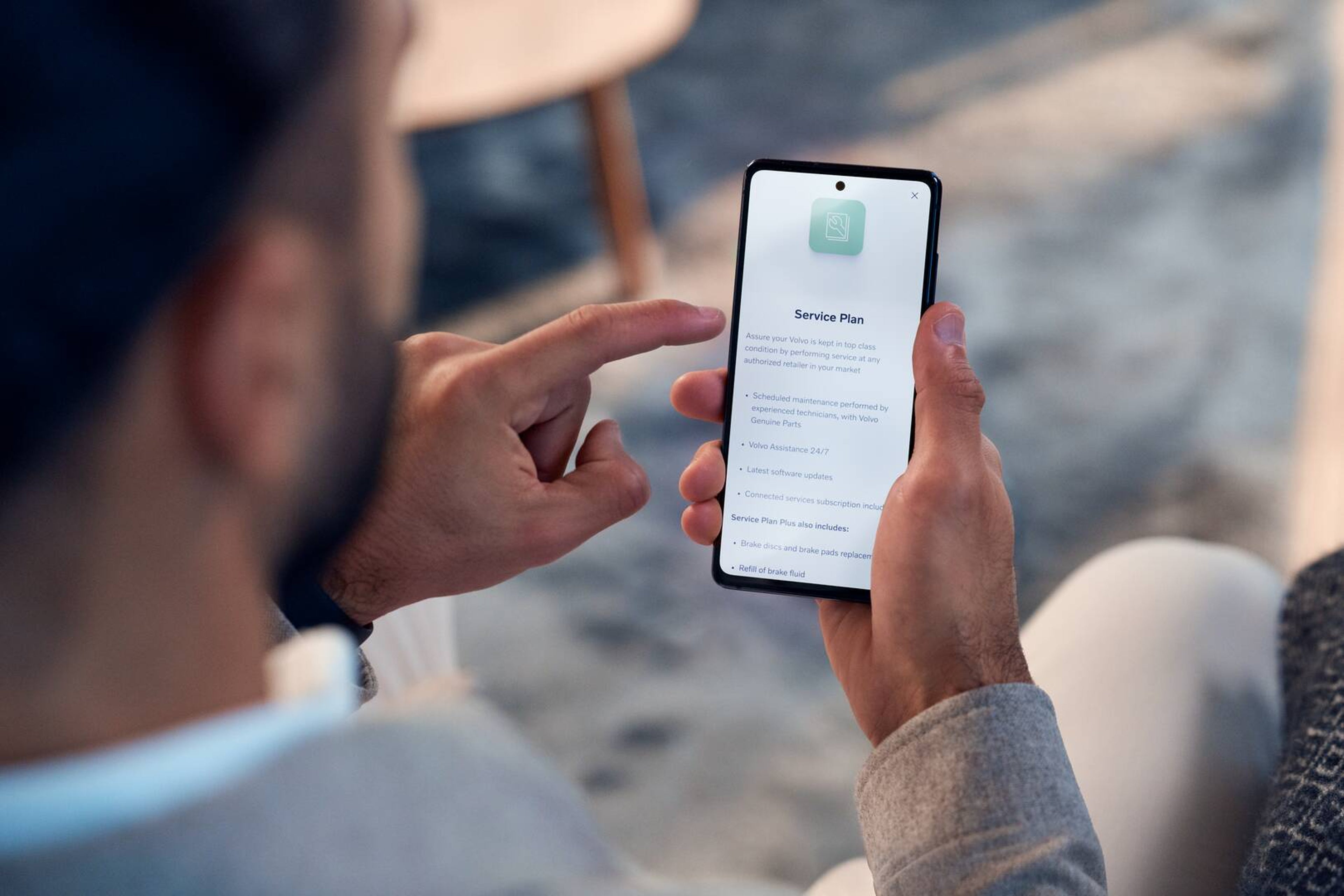 En person holder en smartphone, der viser en "Serviceaftale"-app på skærmen. Stemningen er afslappet og antyder fokus på bilvedligeholdelse eller supporttjenester.