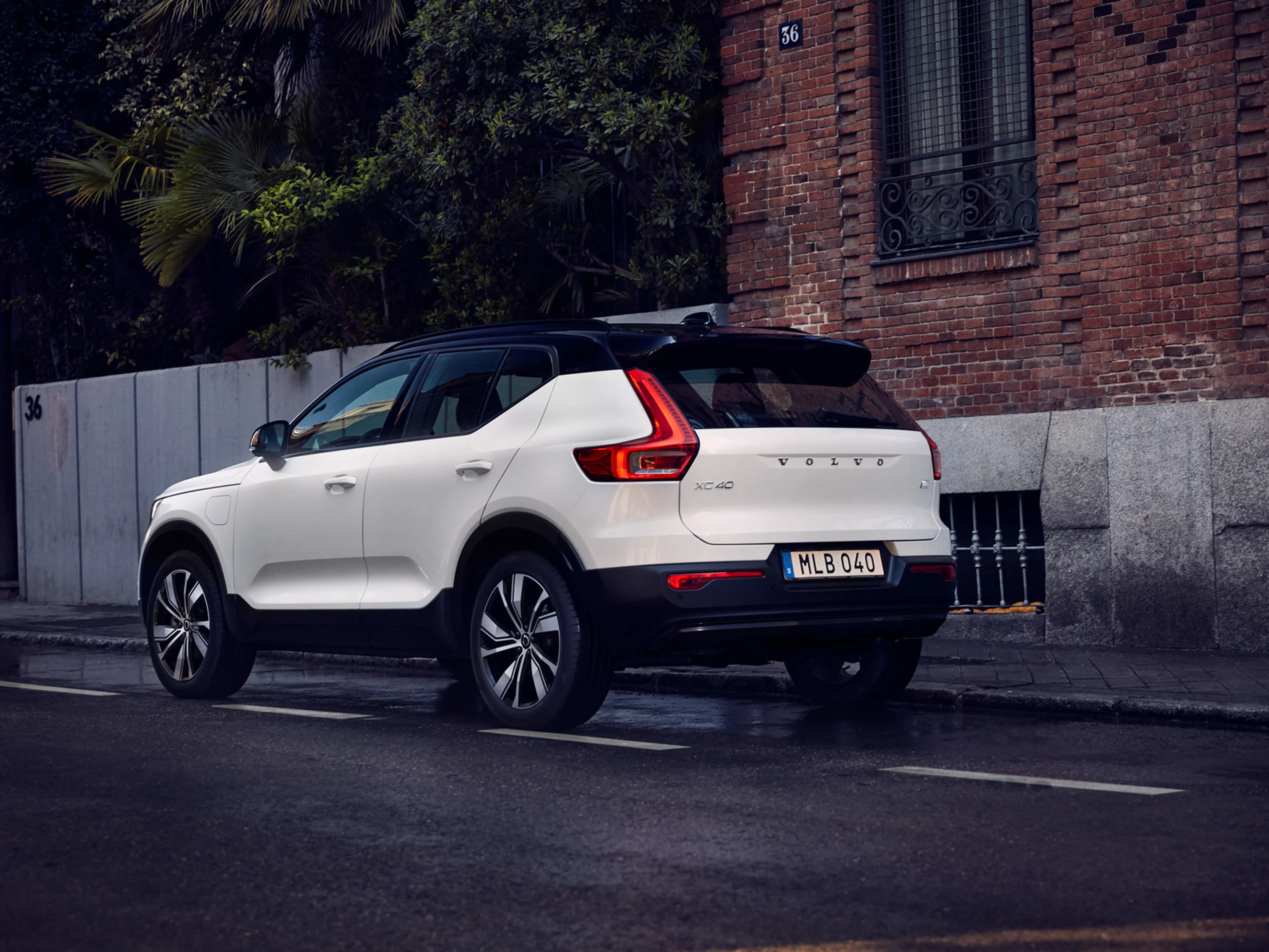 Volvo XC40 branco de perfil numa estrada, com um edificil tijolo e uma vestação densa