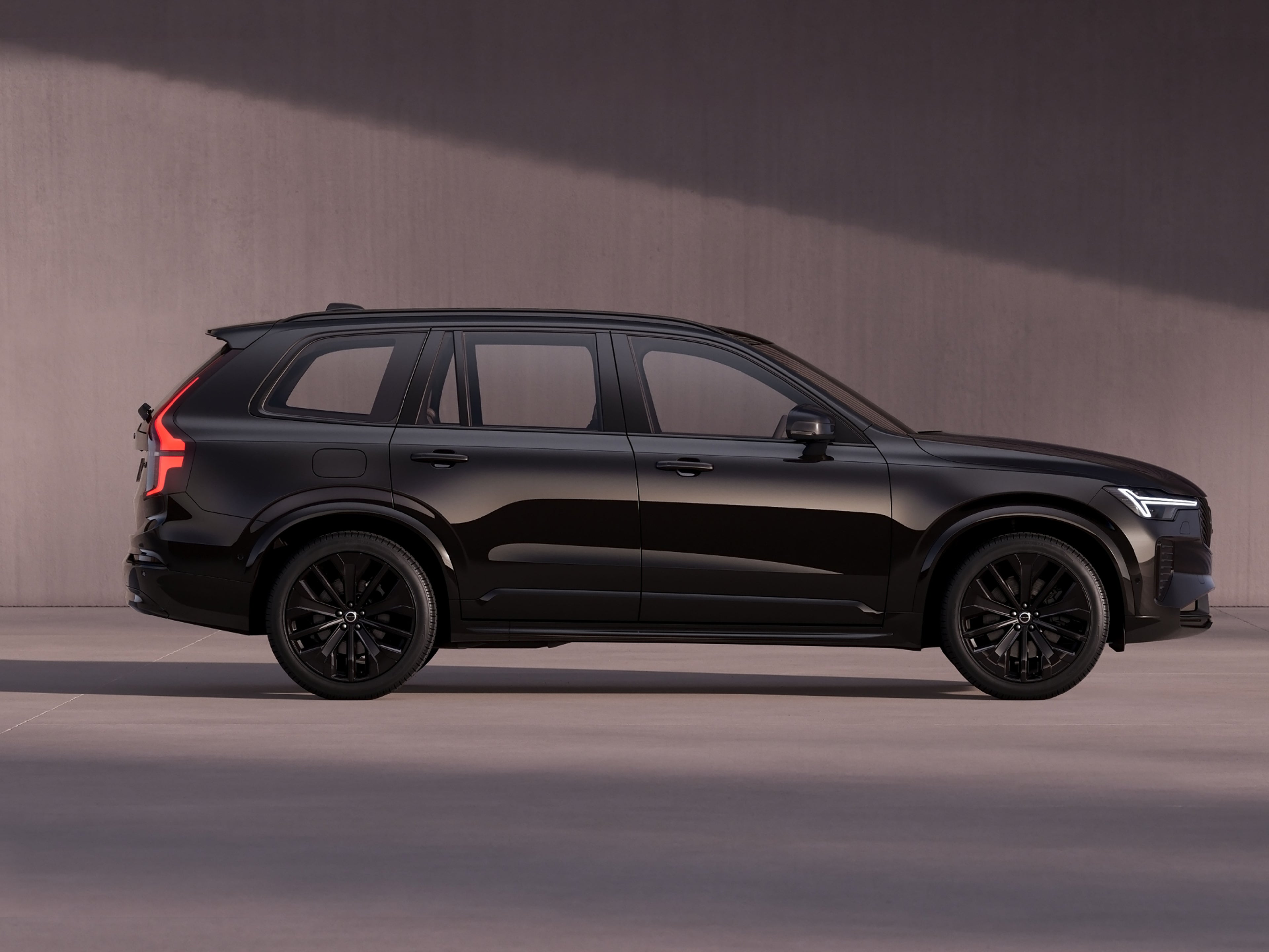 Seitenansicht eines tiefschwarzen Volvo XC90 vor einer dunklen Steinwand.