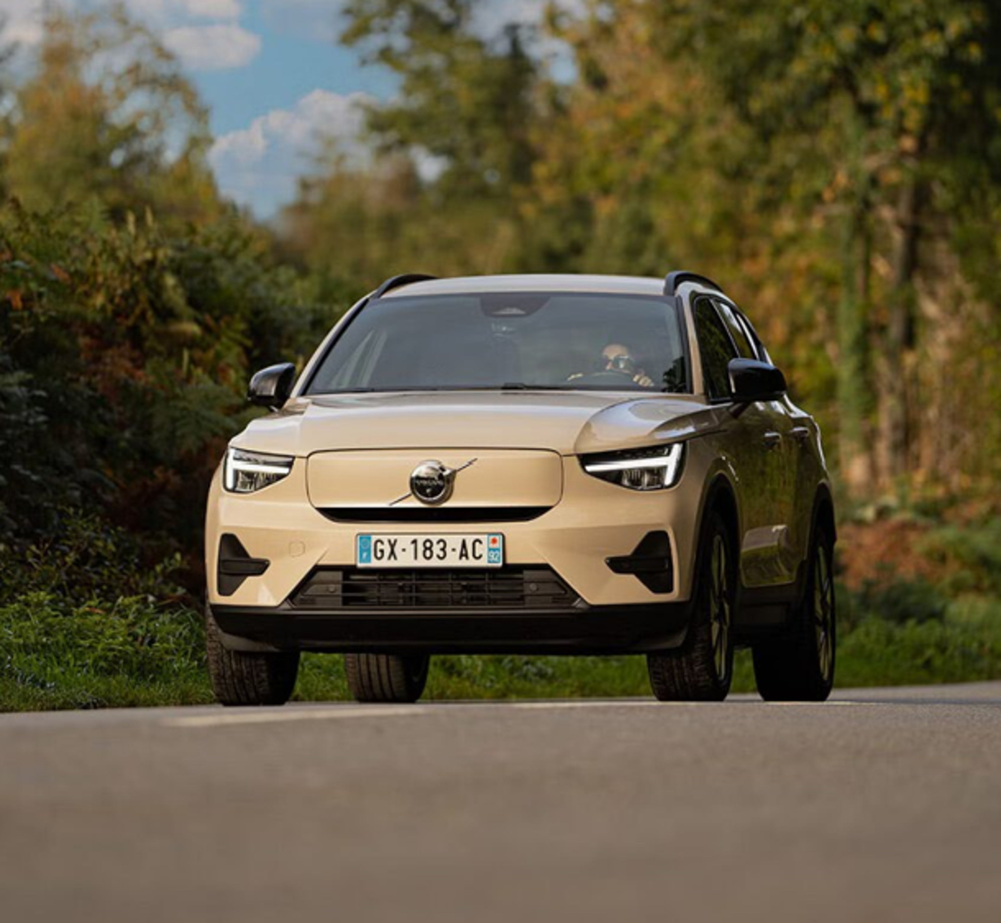 Volvo beige sur route de campagne, plaque GX-183-AC visible, ciel bleu avec quelques nuages.