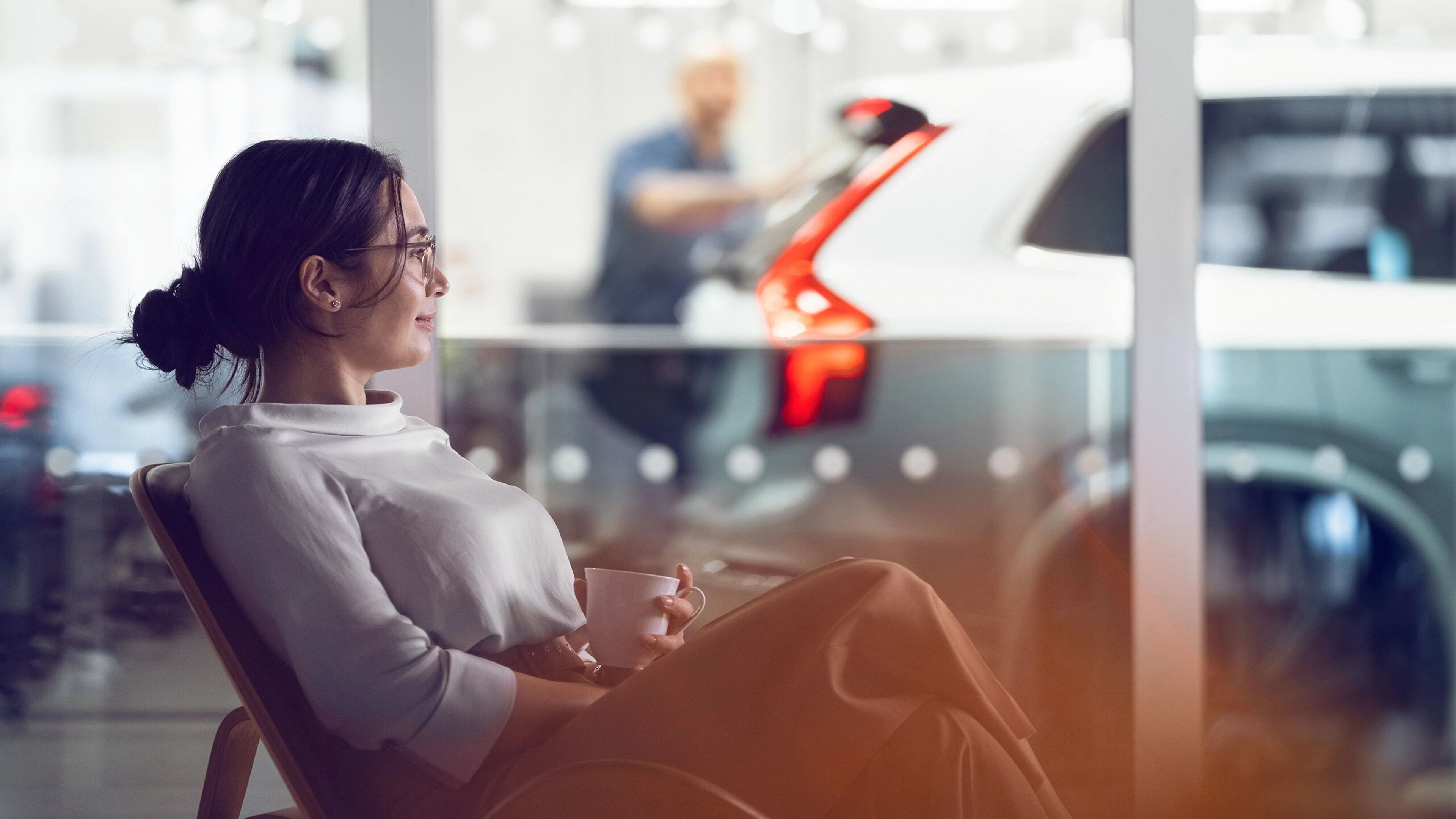 A woman waiting in a Volvo showroom, waiting on her Volvo to be serviced with a coffee in hand.