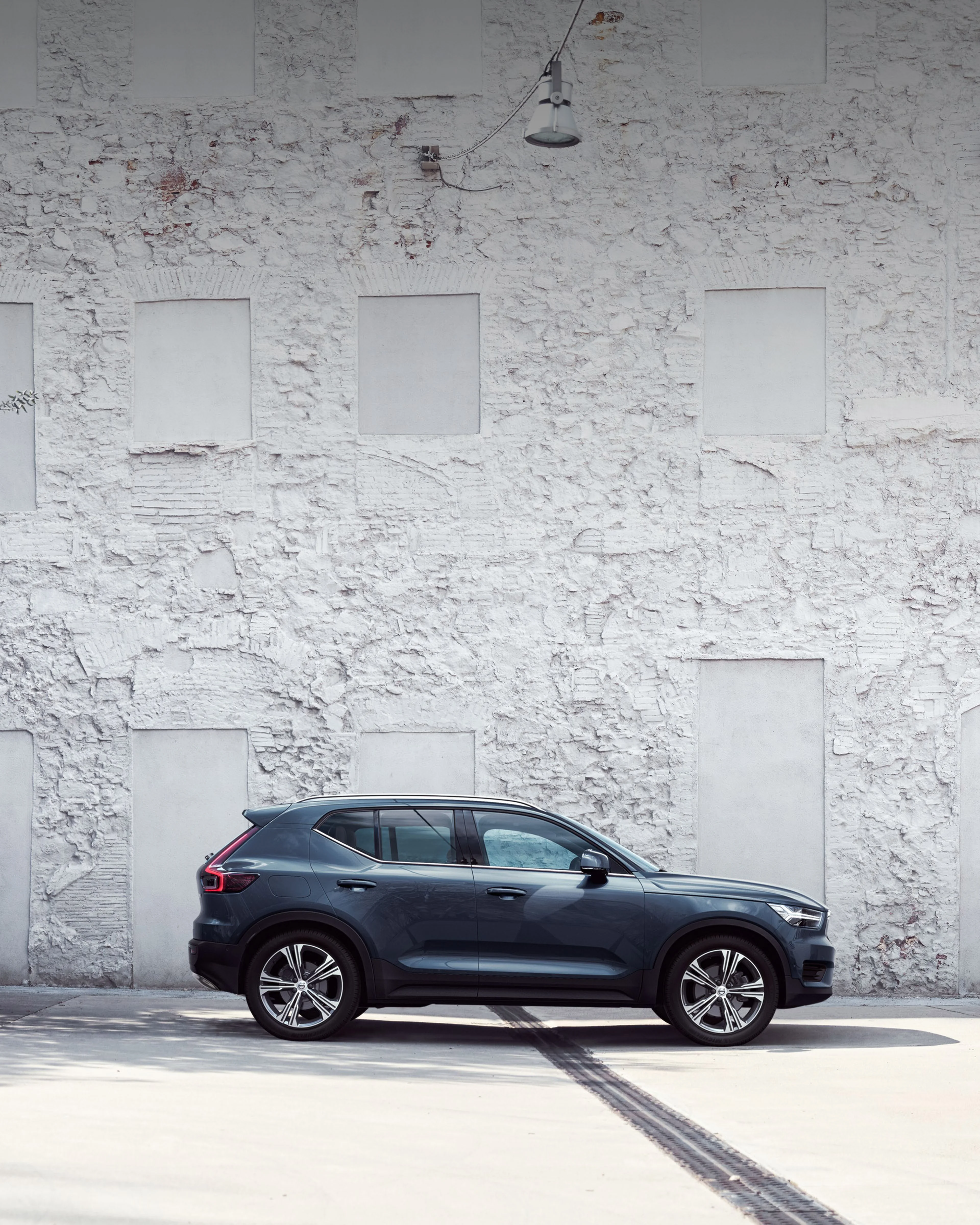Une Volvo XC40 bleue foncée se dresse sur une cour blanche avec 2 sièges.