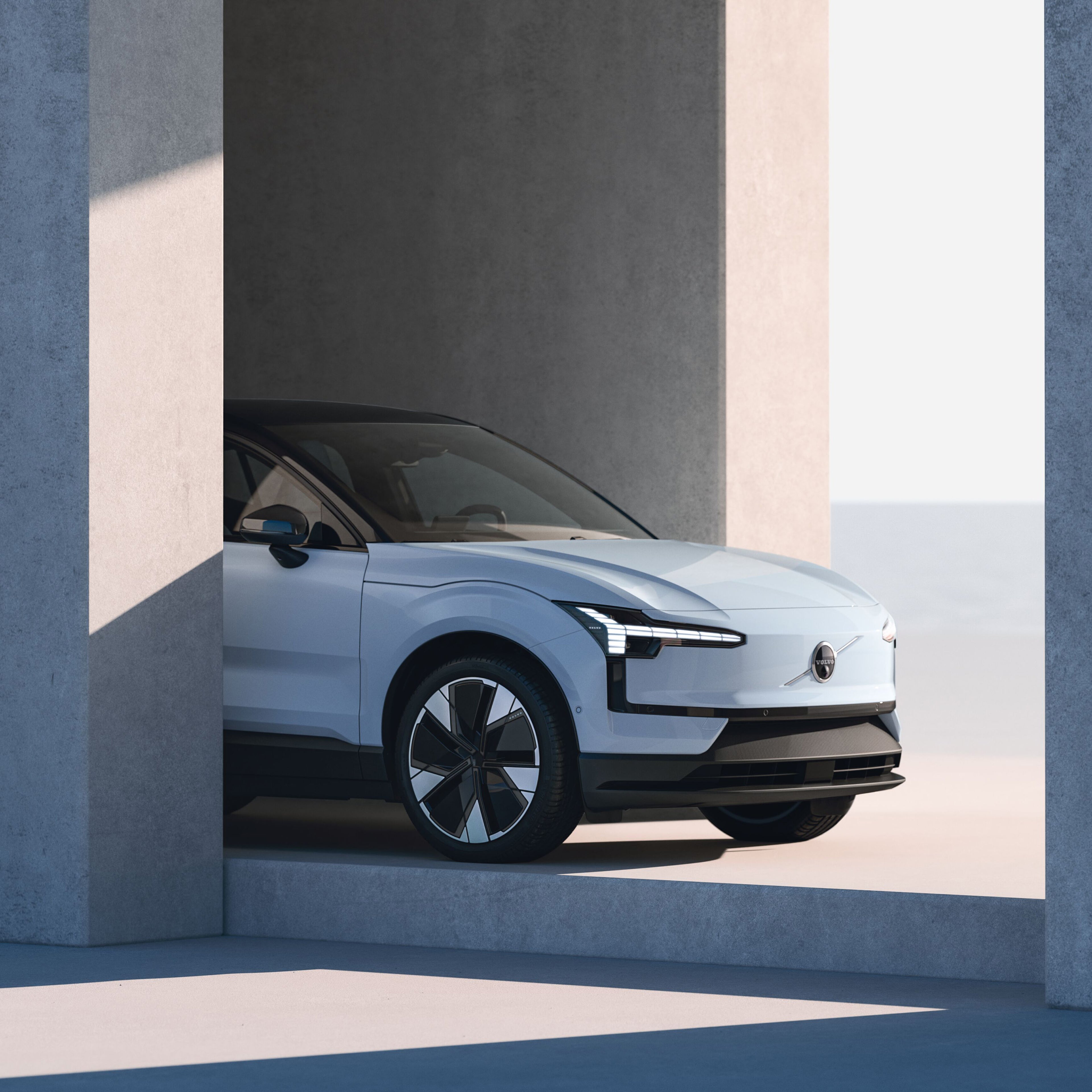 A sleek Volvo EX30, parked in a minimalistic concrete structure, illuminated by soft natural light.
