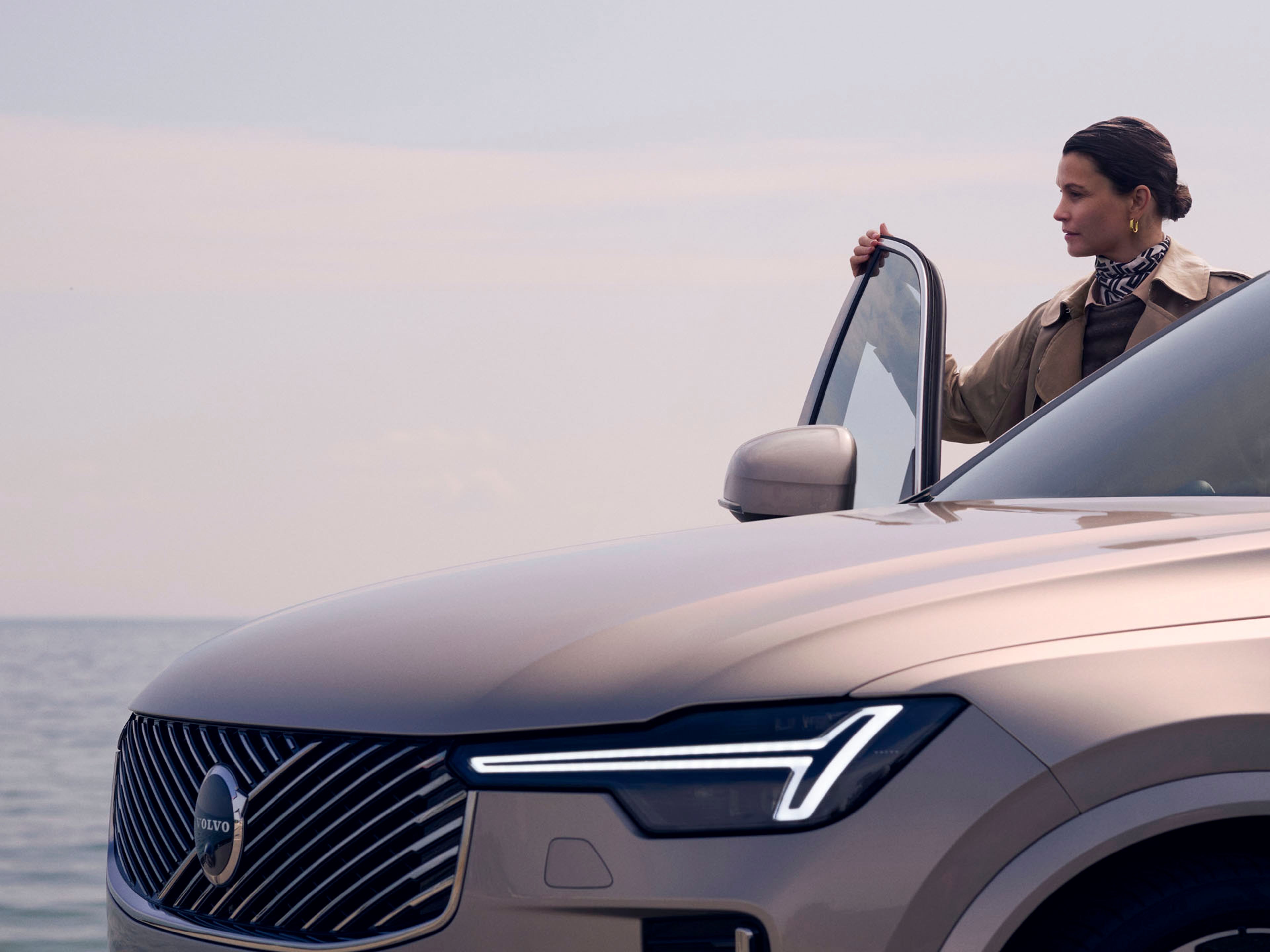 Una mujer de pie junto a un Volvo XC90 híbrido enchufable con la puerta abierta