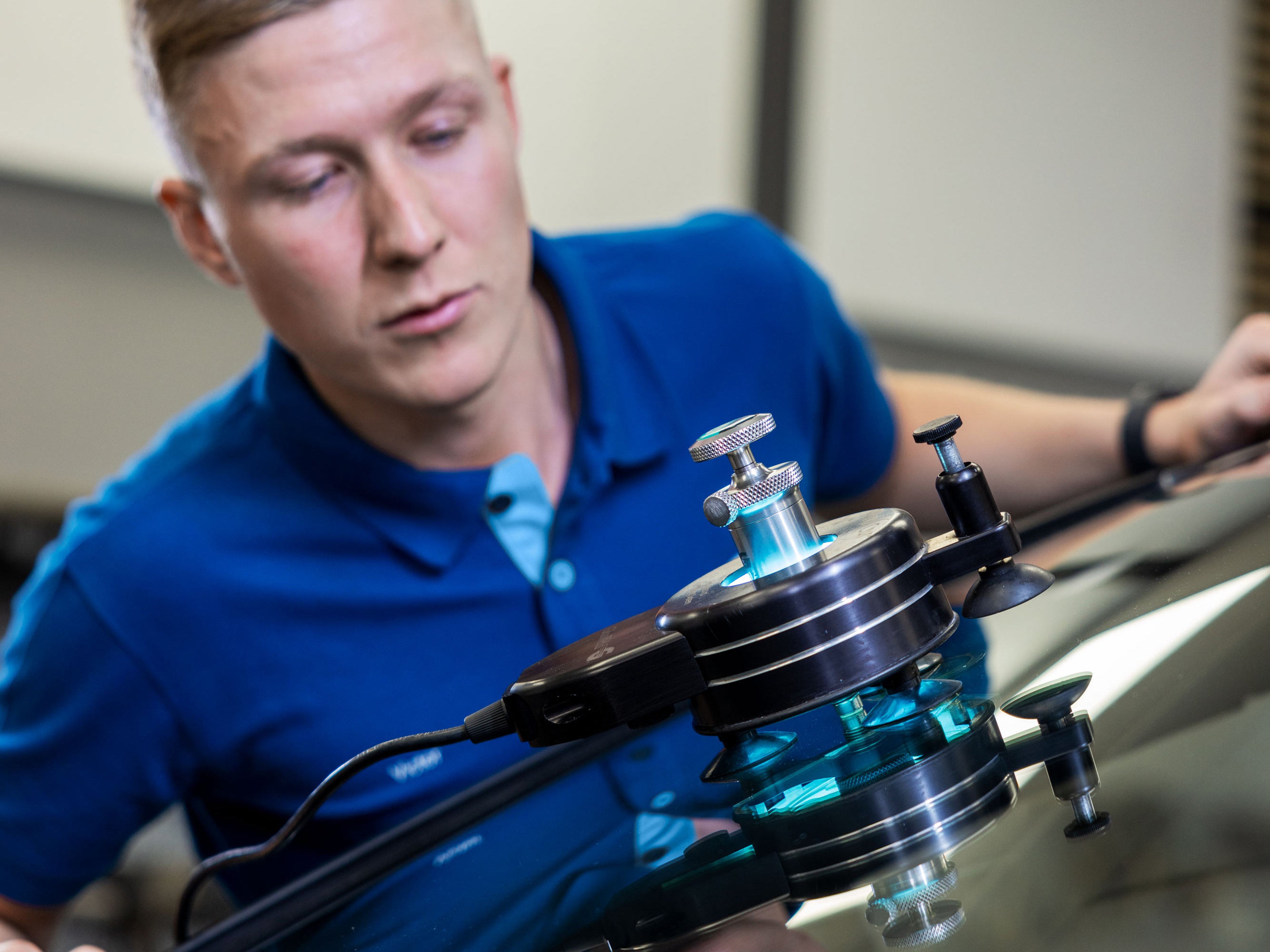 Un technicien répare un impact sur le pare-brise d'une Volvo à l'aide d'un équipement spécial qui émet une lumière bleue.