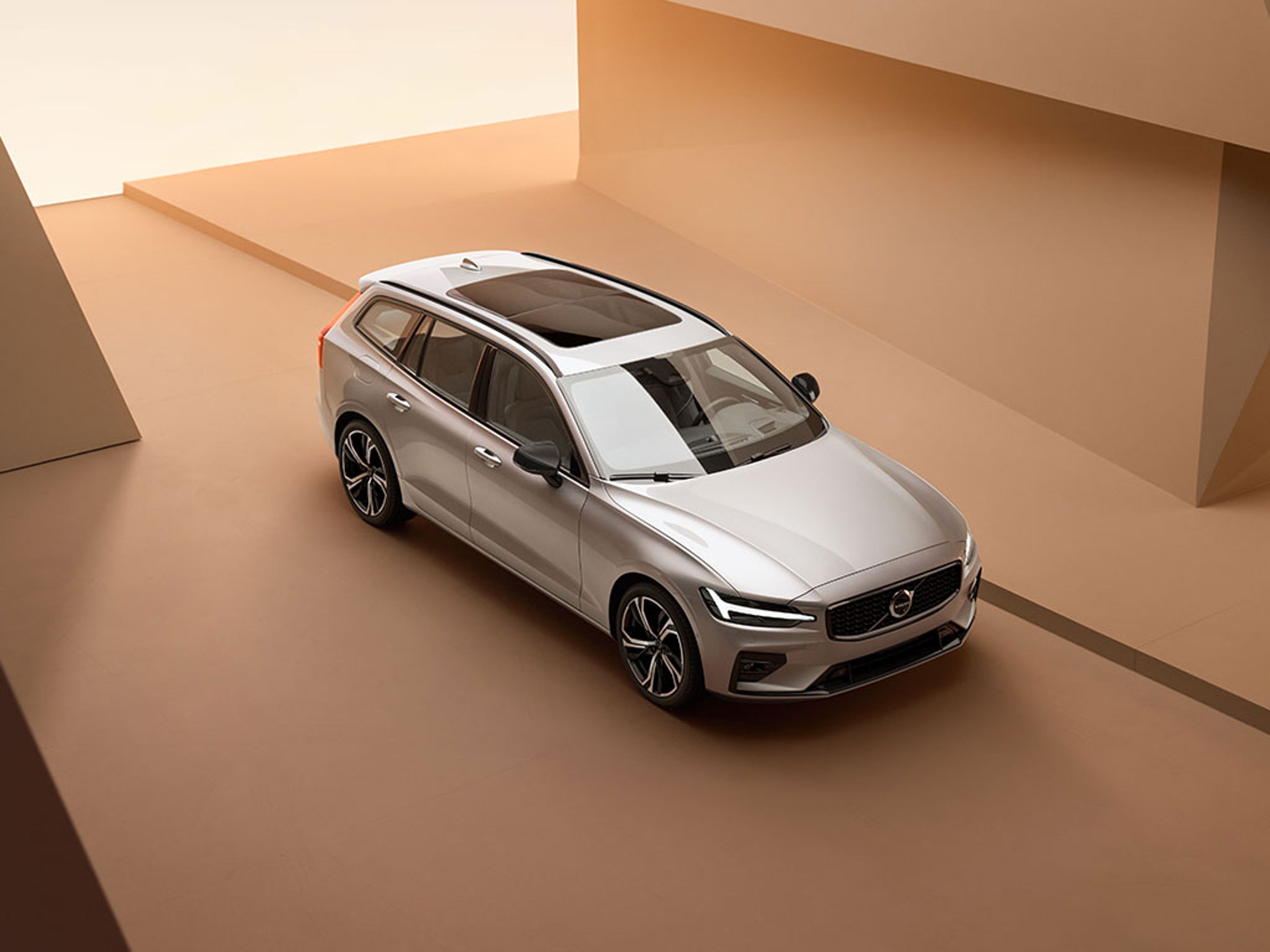 Vue de haut d’un break Volvo V60 gris argent dans un univers orangé architectural et minimaliste