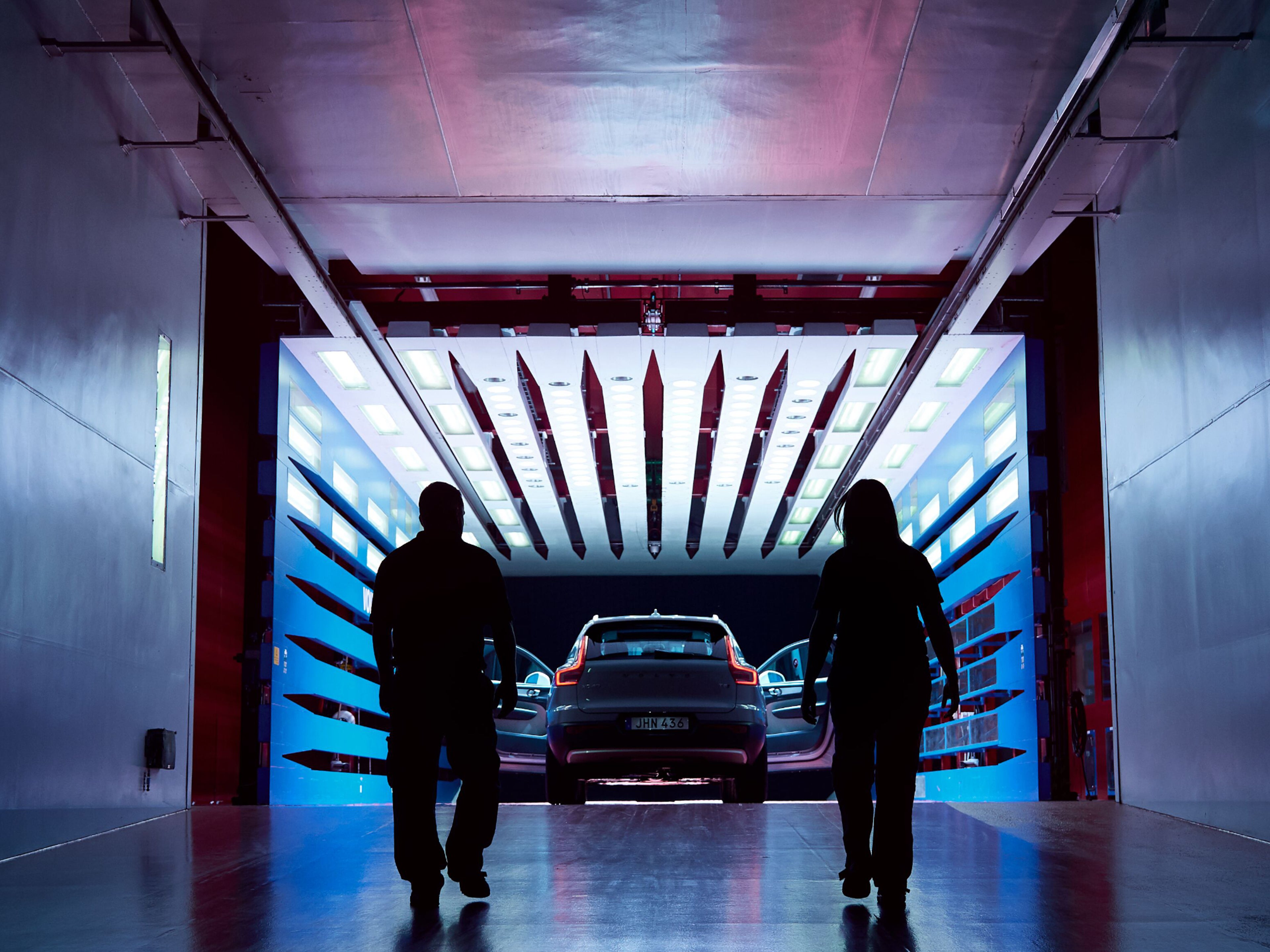 Zwei Personen gehen auf einen Volvo zu, der in einem Windtunnel mit zwei geöffneten Türen steht.