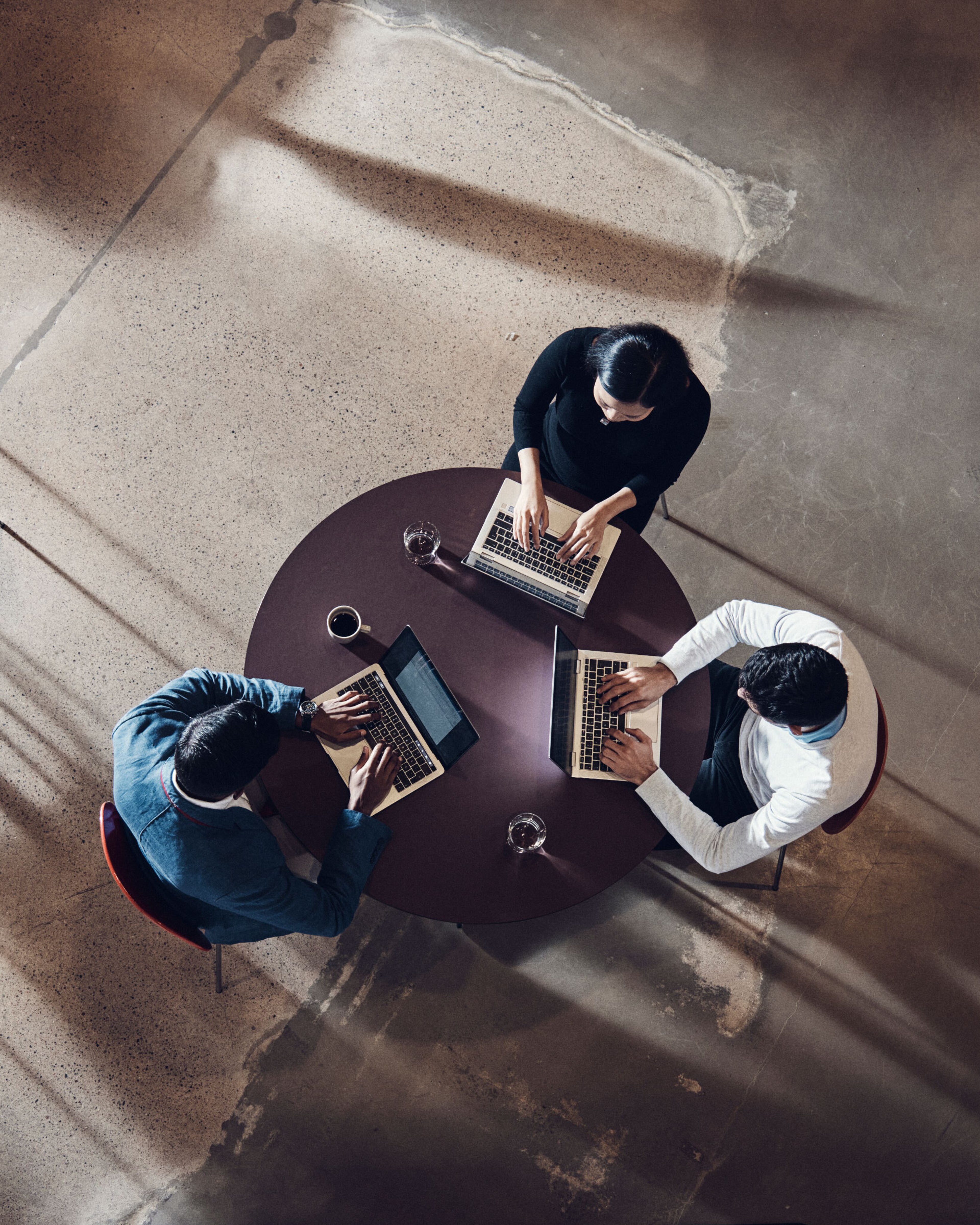Drei Menschen sitzen an einem Tisch und arbeiten an Laptops.