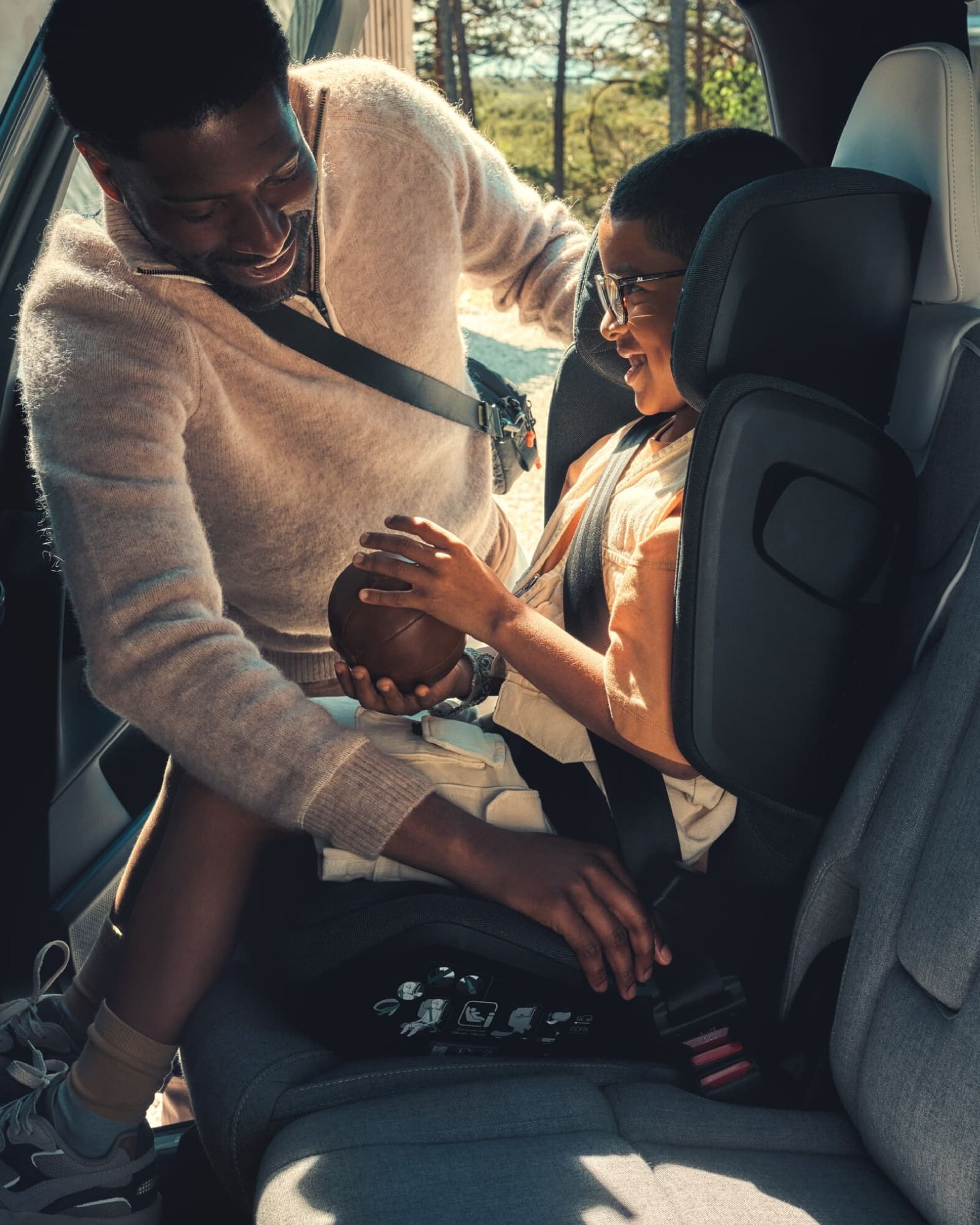 Een vader helpt zijn zoon in een autostoel op de achterbank van een auto.