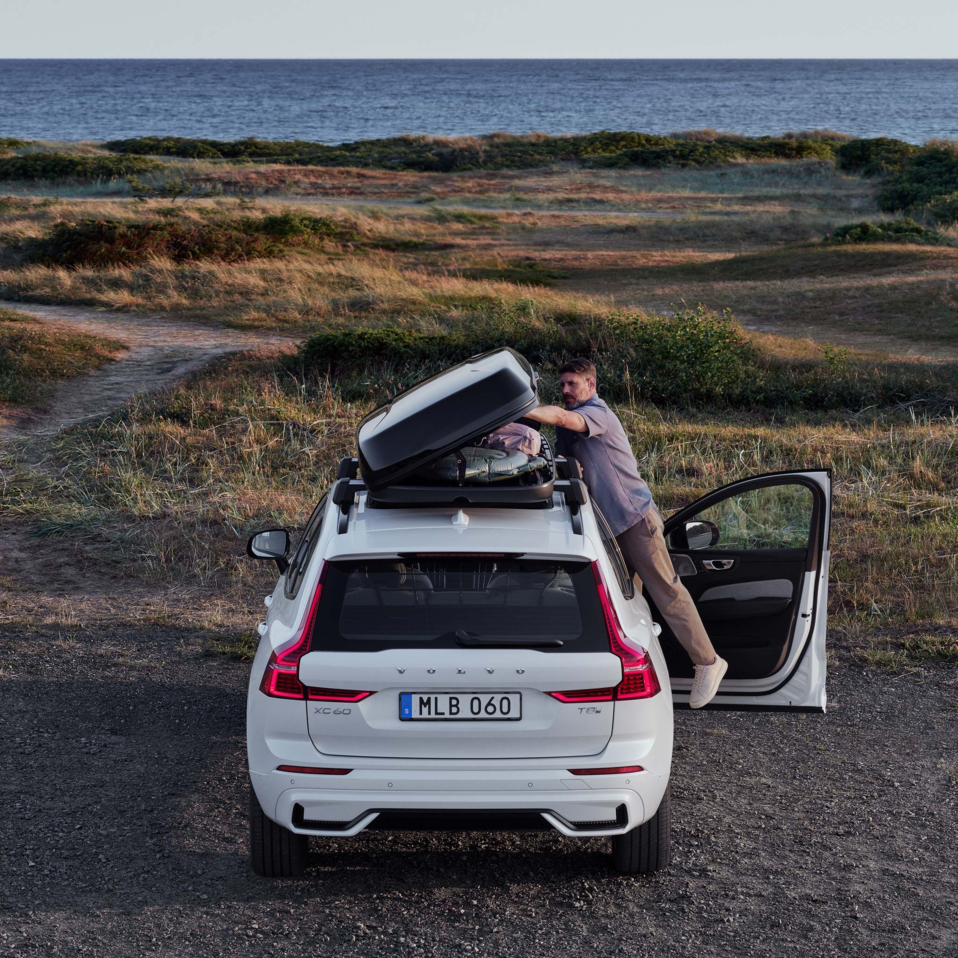 Mies lastaa merenrantaan pysäköidyn Volvo XC60 lataushybridiauton kattolaatikkoa.