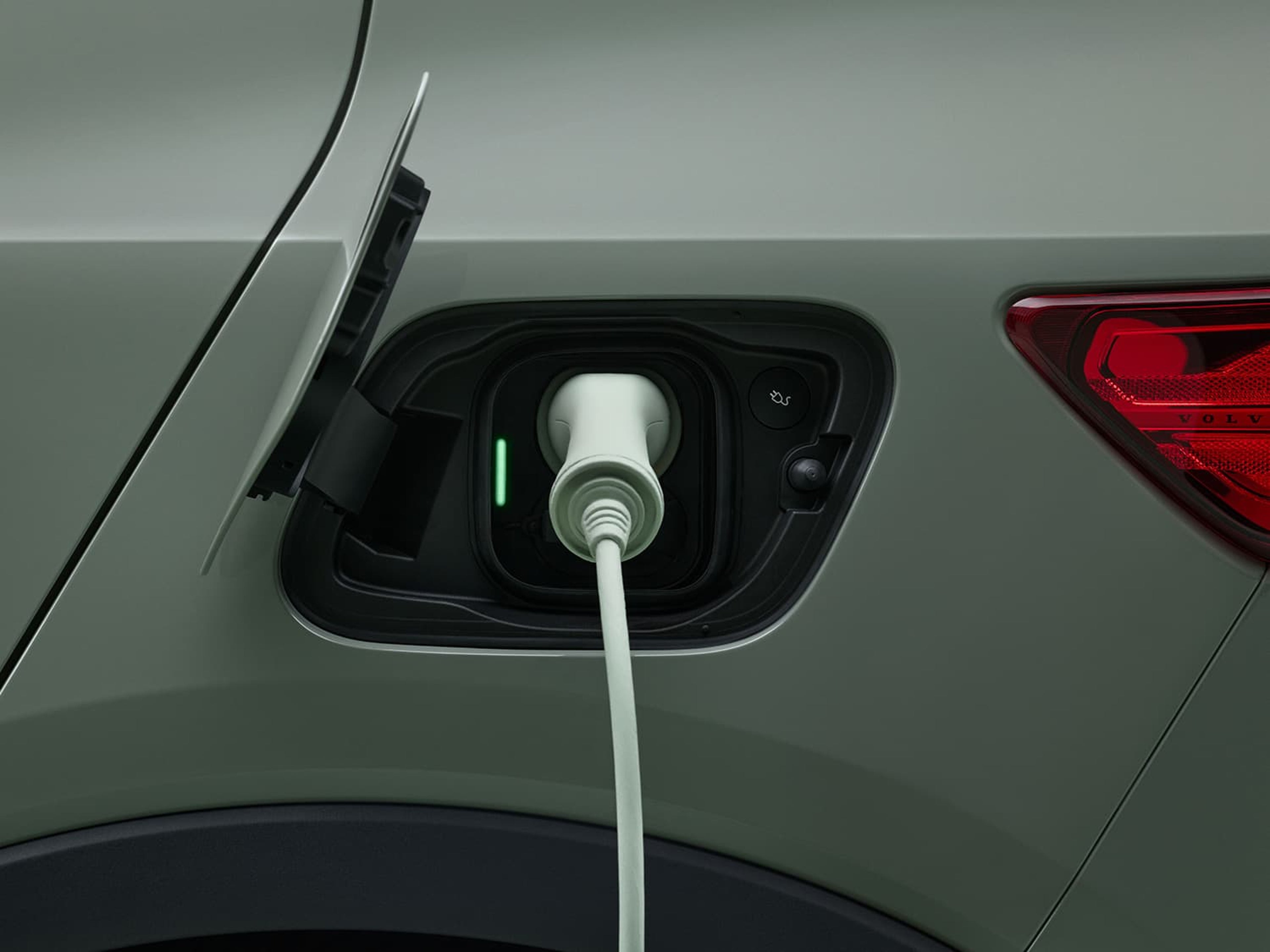 Gros plan du port de recharge d'une voiture Volvo électrique, avec le câble de recharge branché et un voyant vert indiquant que la voiture est en charge.