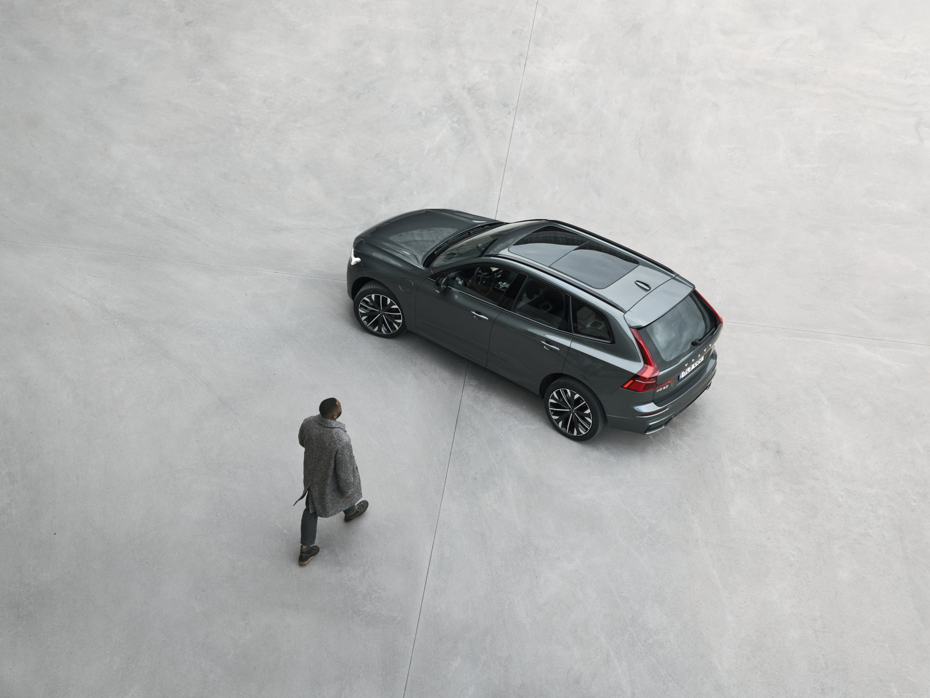 Top down view of person in long coat walking towards their Volvo XC60 on plain grey surface
