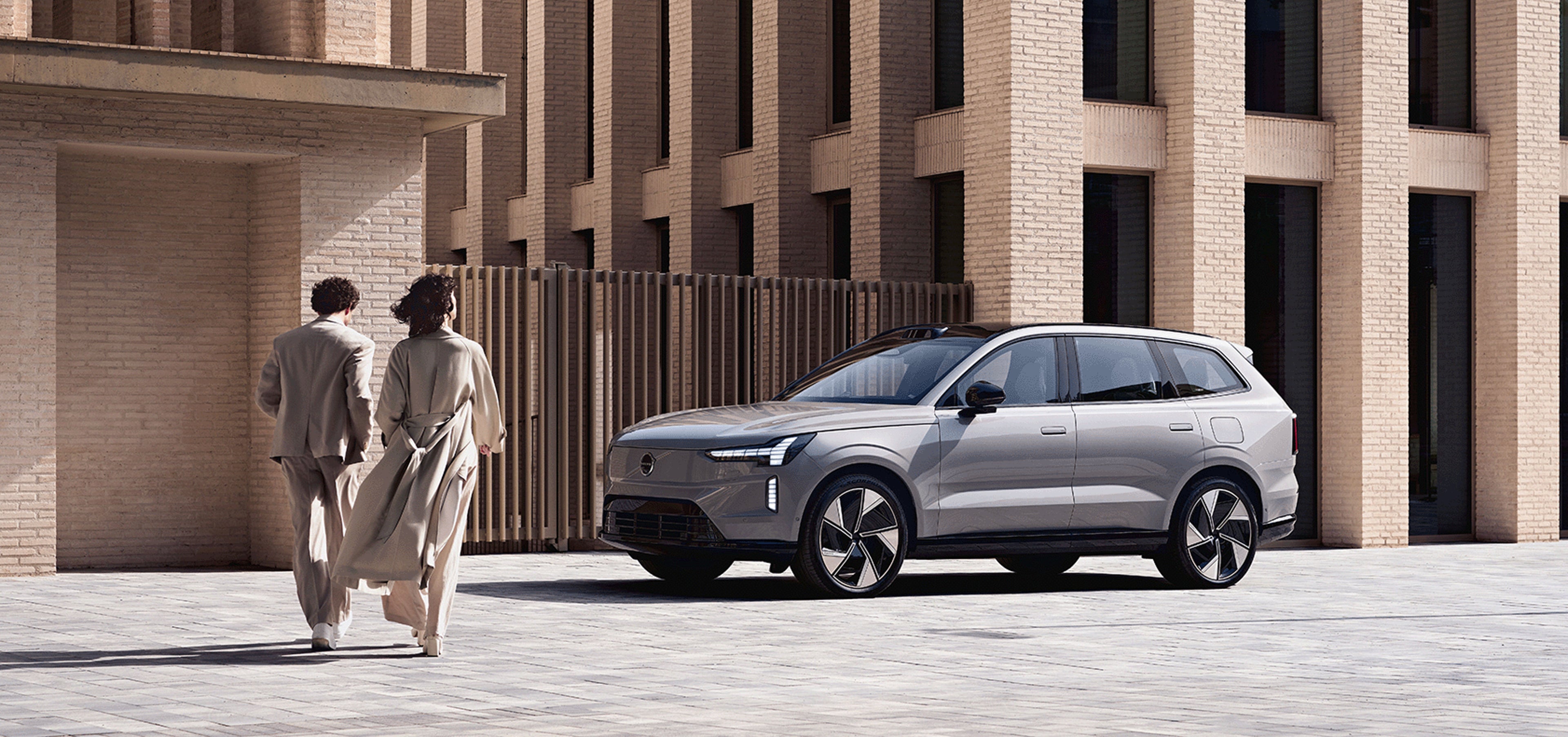 Zwei Menschen laufen auf einen Volvo EX90 zu.