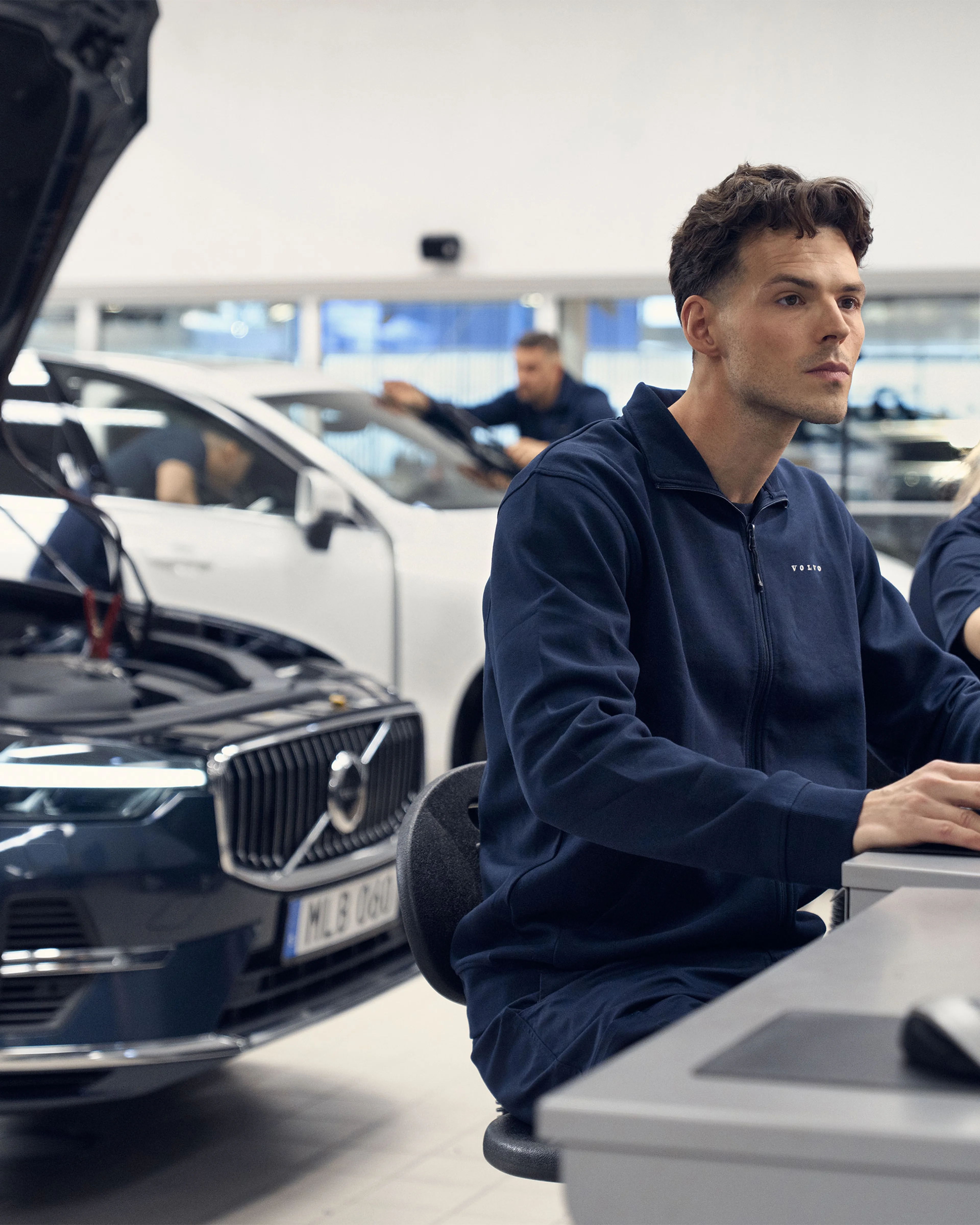 Un technicien devant son ordinateur inspecte le boitier informatique du Volvo XC60 placé derrière lui avec le capot ouvert