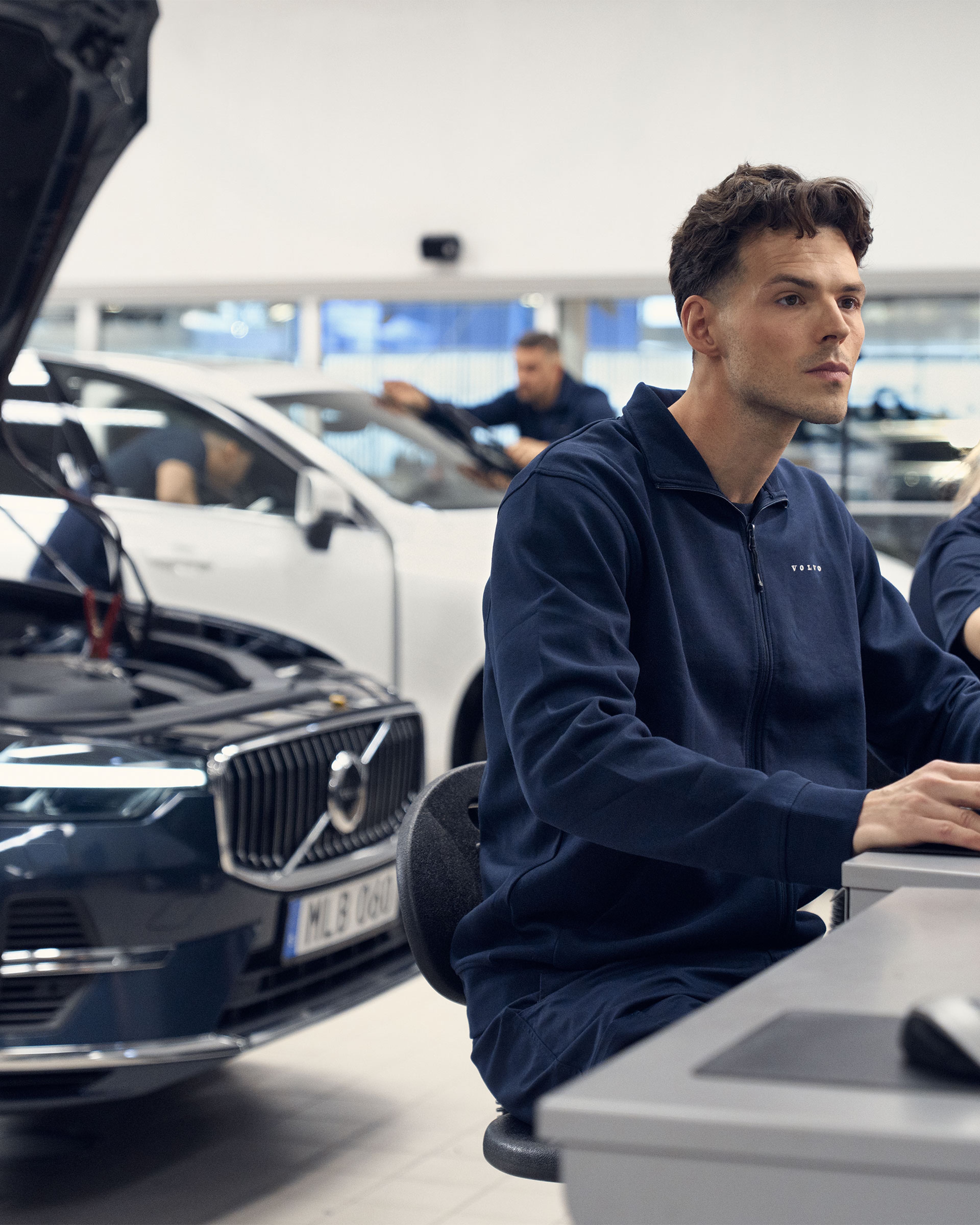 Un technicien devant son ordinateur inspecte le boitier informatique du Volvo XC60 placé derrière lui avec le capot ouvert