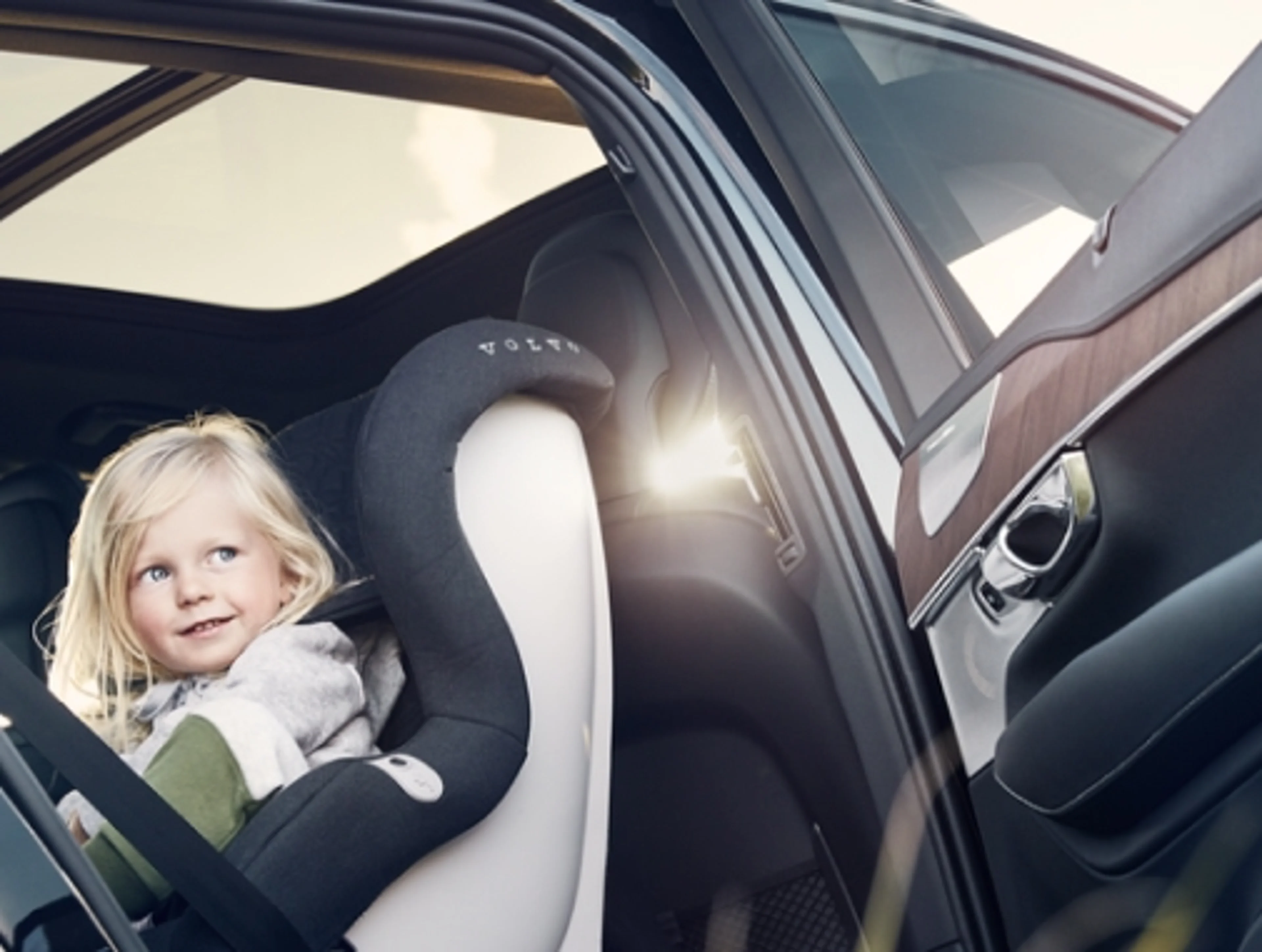 Een kind met blond haar zit vastgemaakt op een Volvo kinderzitje op de achterbank.