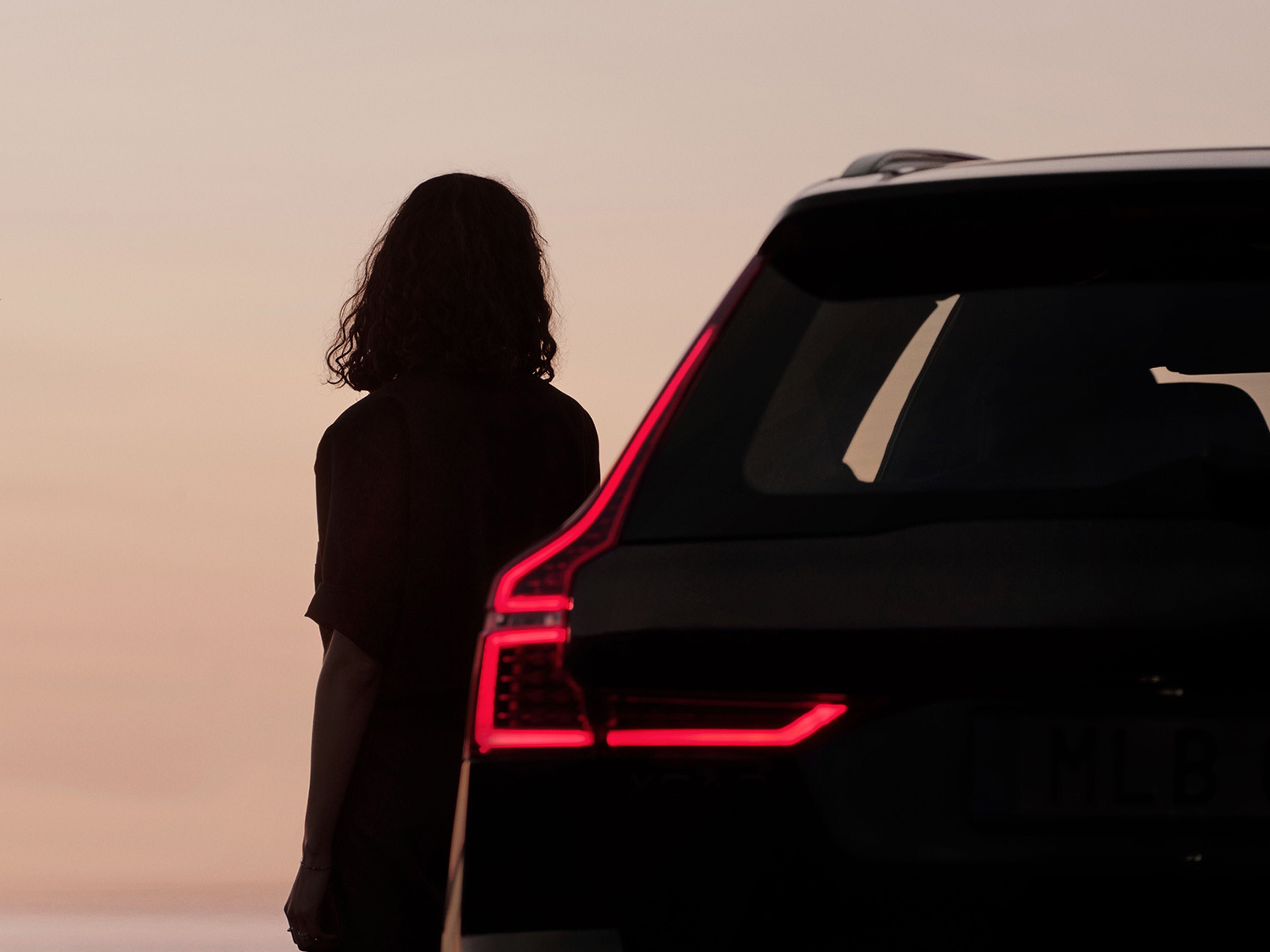 Silhouette d'une personne debout à côté d'une Volvo XC40, avec un éclairage d'accentuation rouge visible.