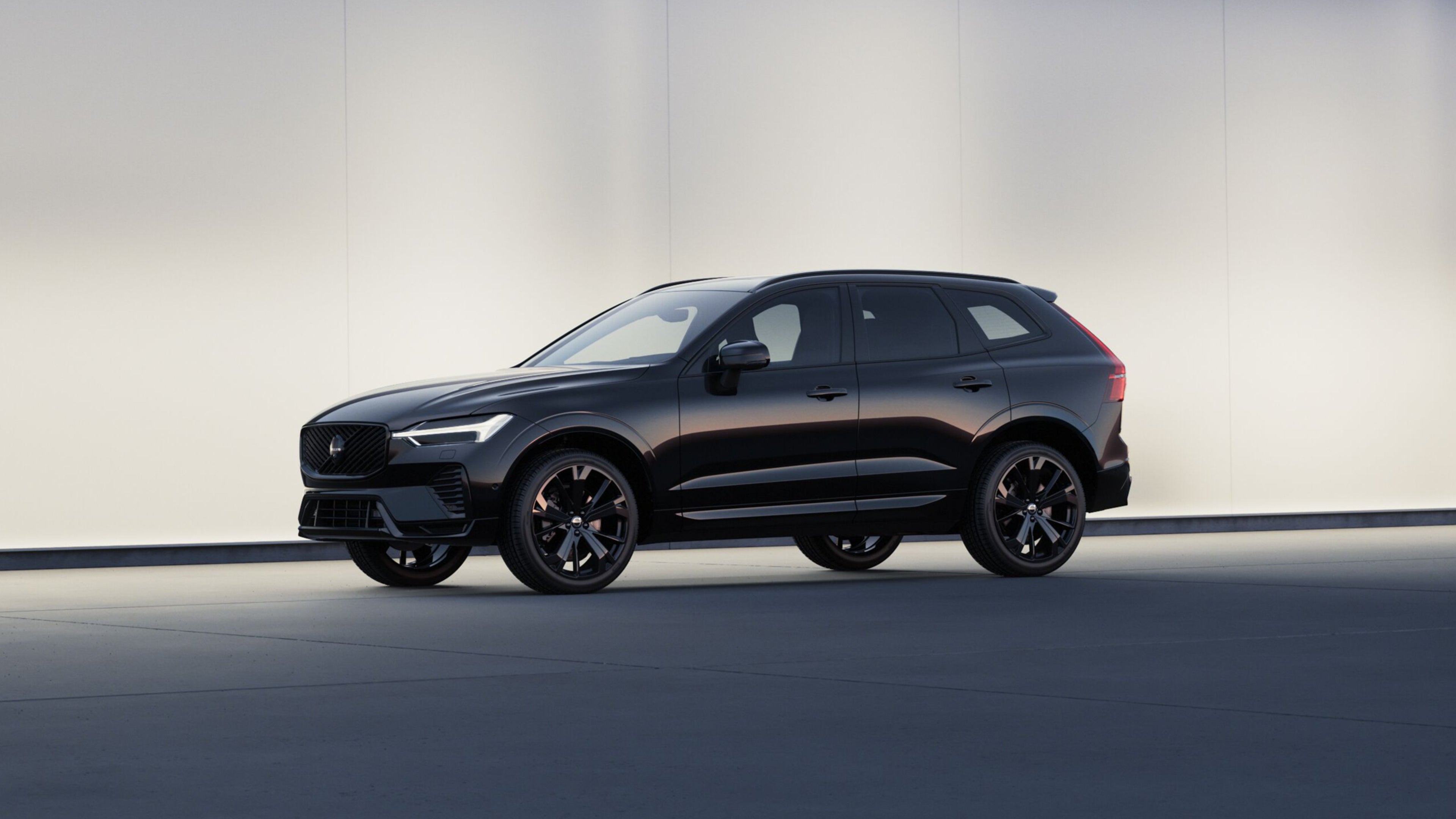 Seitenansicht eines tiefschwarzen Volvo XC60 vor einer hellen Steinwand.