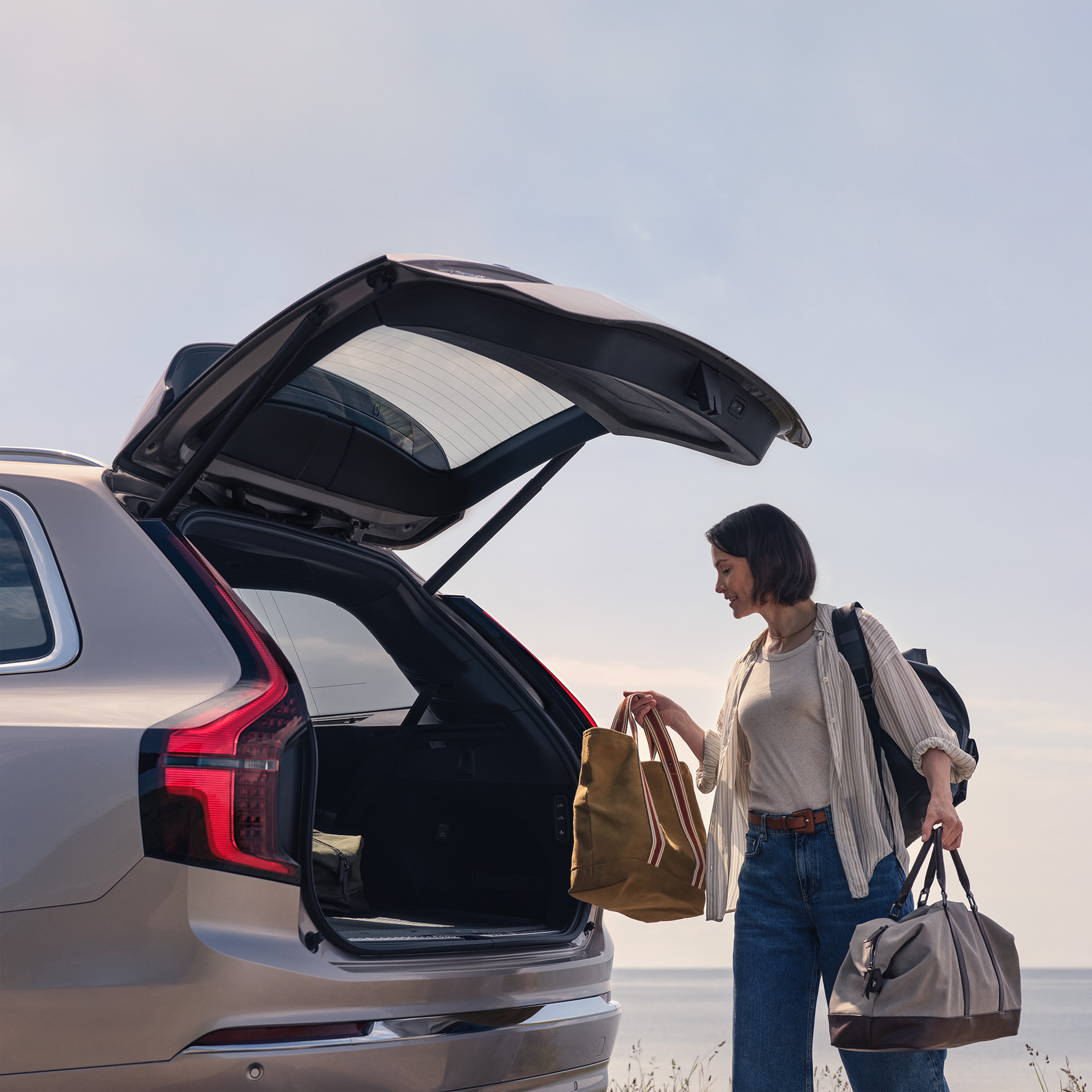 Nainen lastaa laukkuja avoinna olevaan XC90 lataushybridin takatilaan.