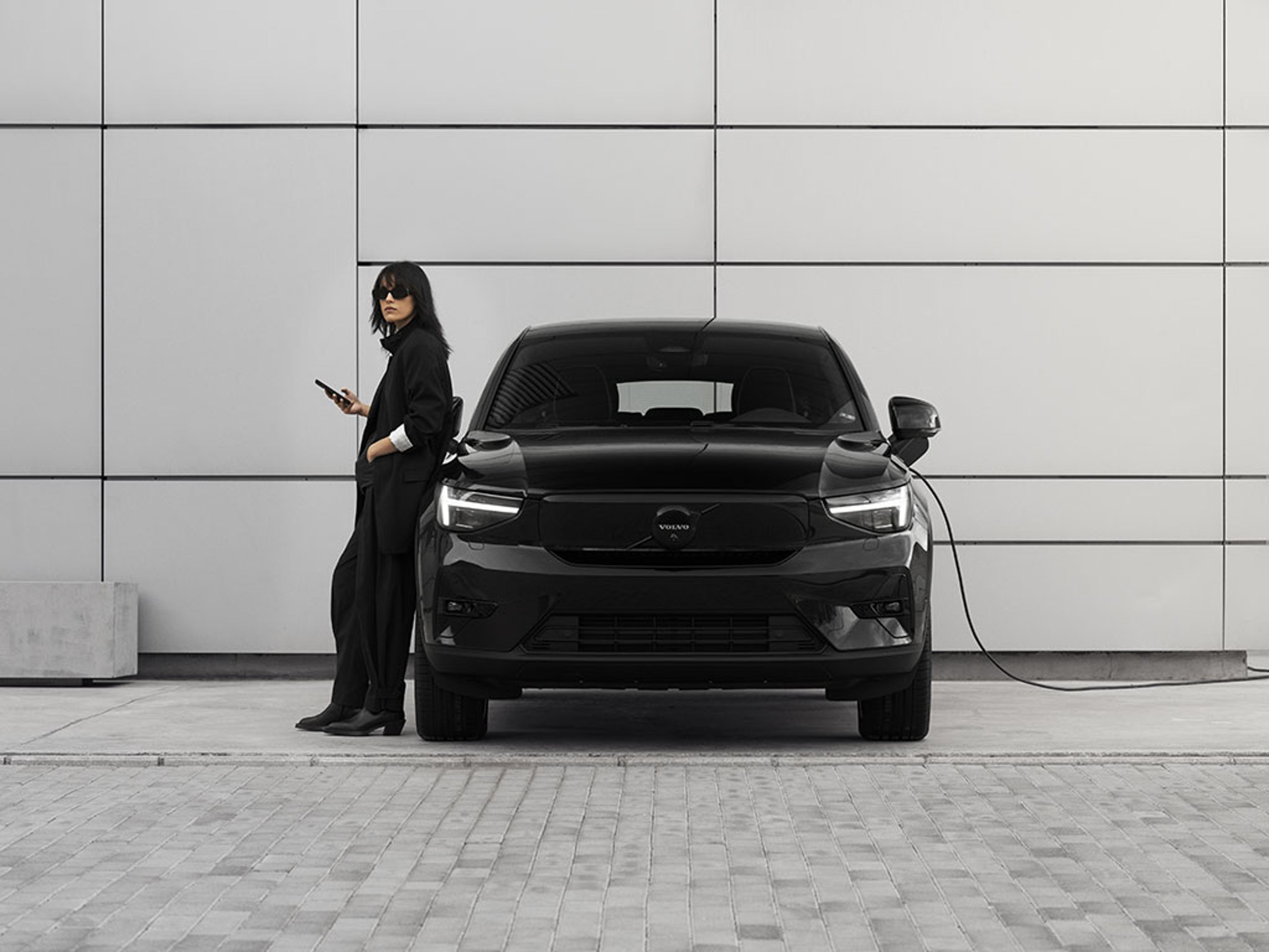 Femme à côté d’un EC40 Black Edition noir en charge devant un bâtiment moderne aux grandes dalles blanches