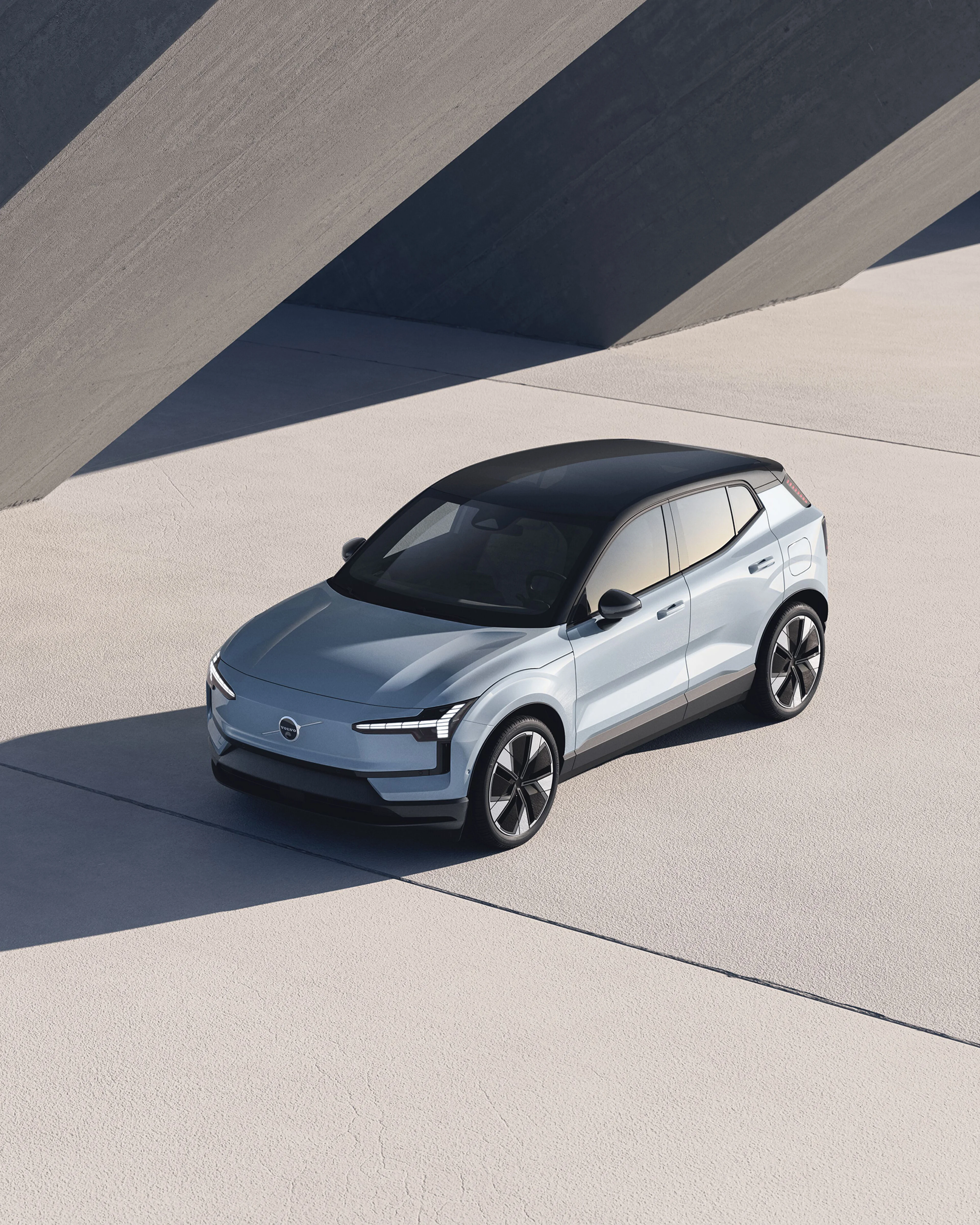 En elegant sølvfarvet Volvo SUV med futuristisk design står på en betonflade, hvor det skrånende sollys kaster skarpe skygger. Scenen udstråler en moderne, minimalistisk og sofistikeret stemning.