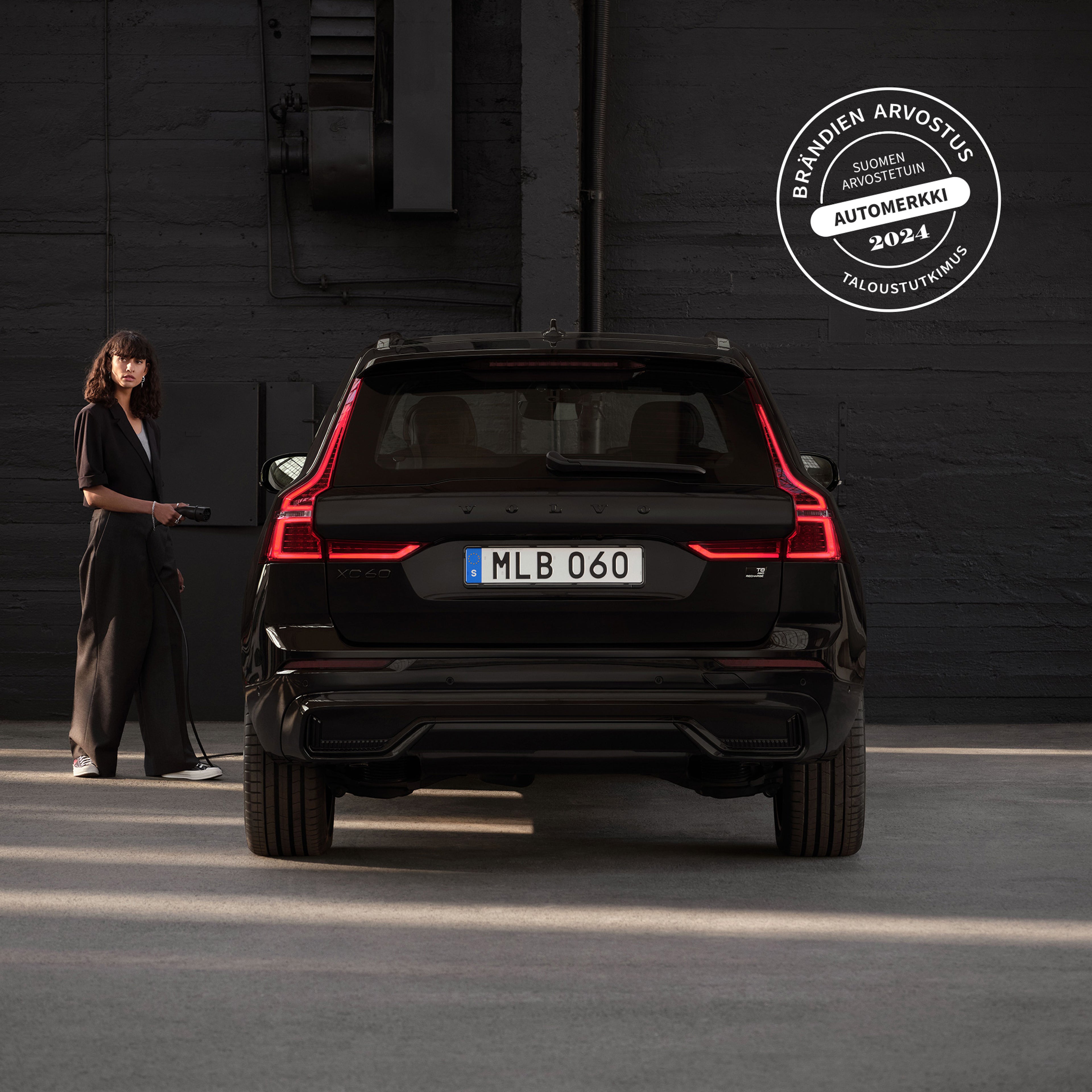 Mustiin pukeutunut nainen ja Volvo XC60 Black Edition -lataushybridi takaa päin kuvattuna.