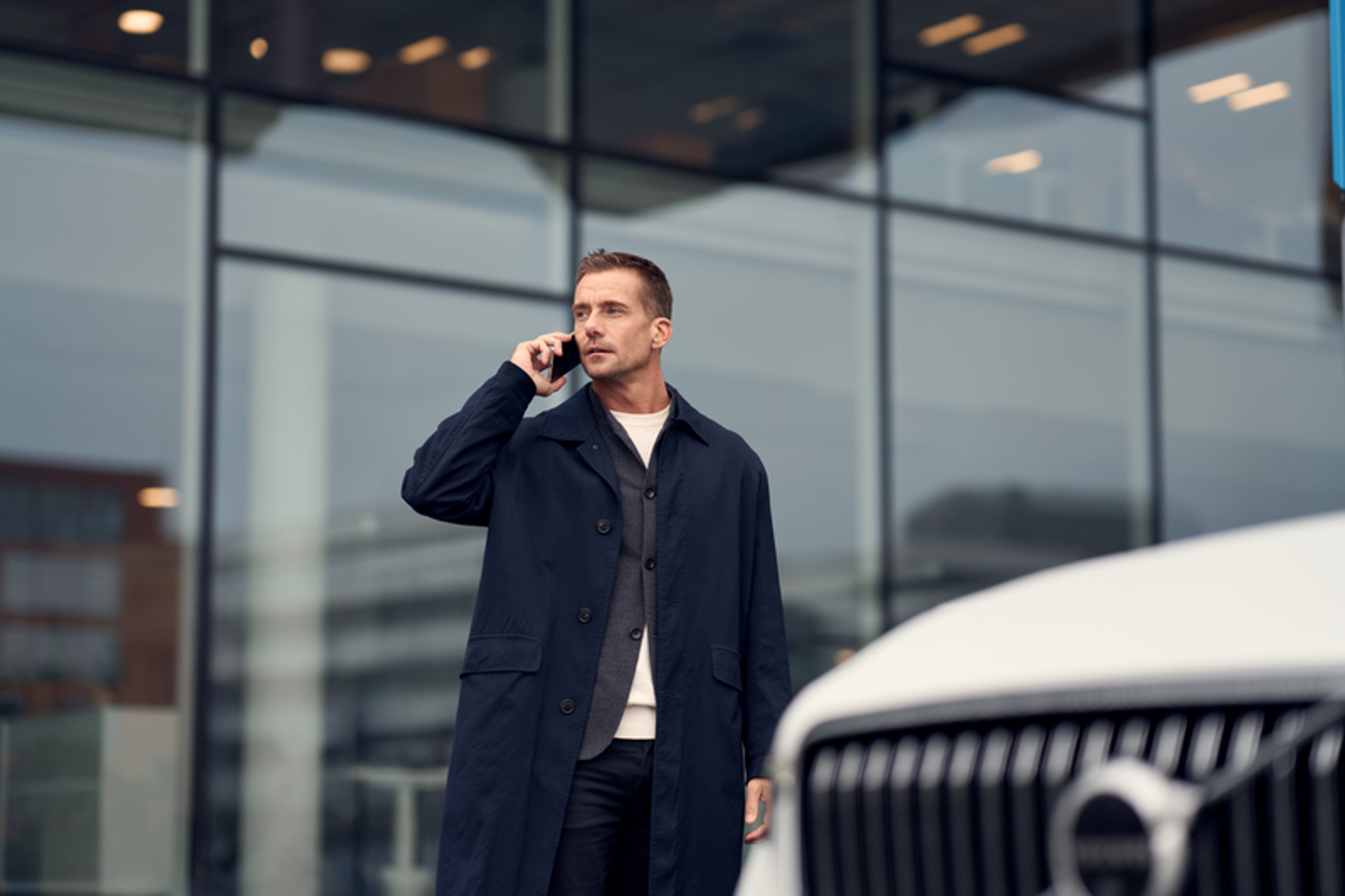 Mężczyzna rozmawiający przez telefon przy Volvo, na tle budynku