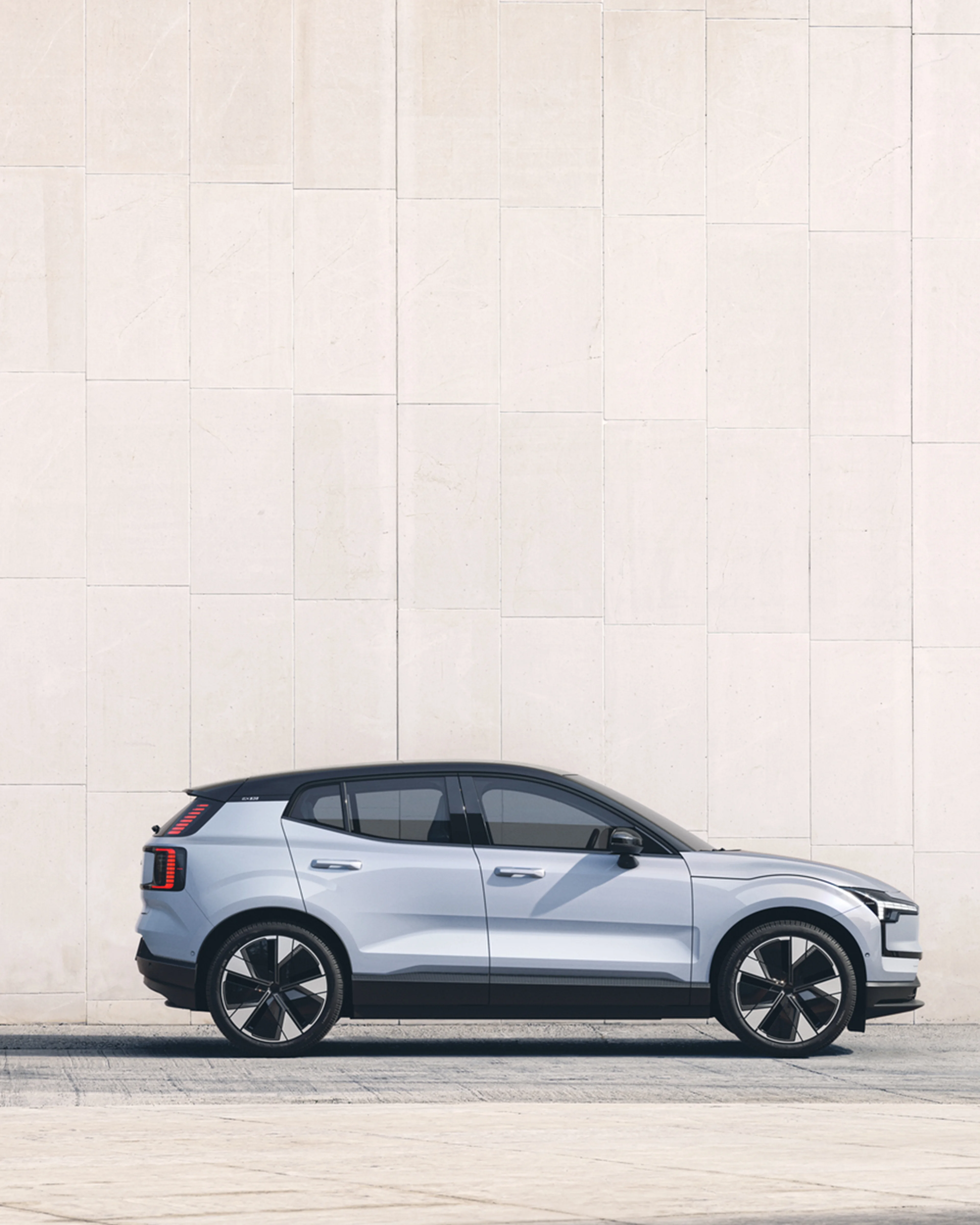 Silvrig Volvo EX30 från sidan mot beige stenvägg