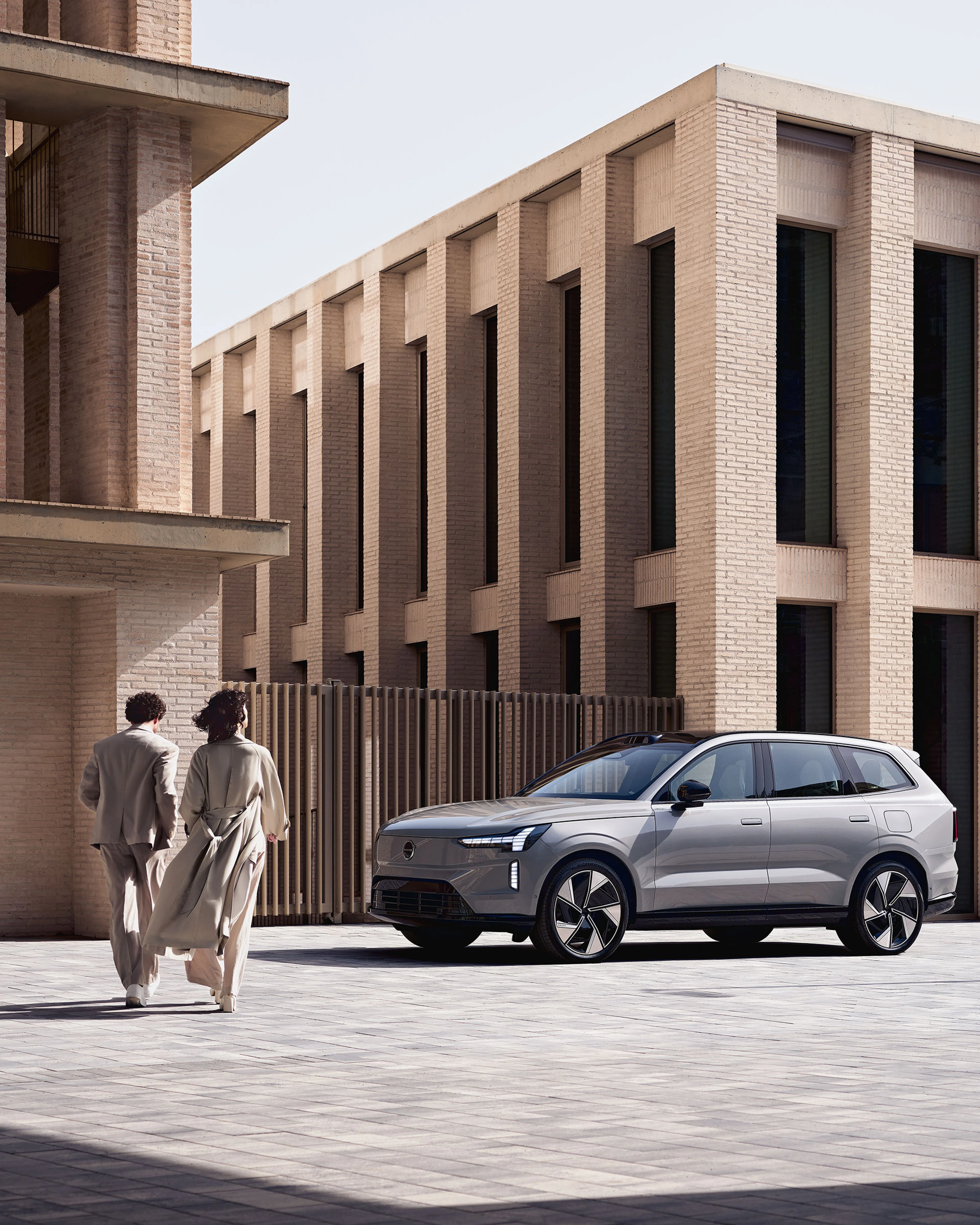 Zwei Personen laufen auf einen Volvo EX90 zu.