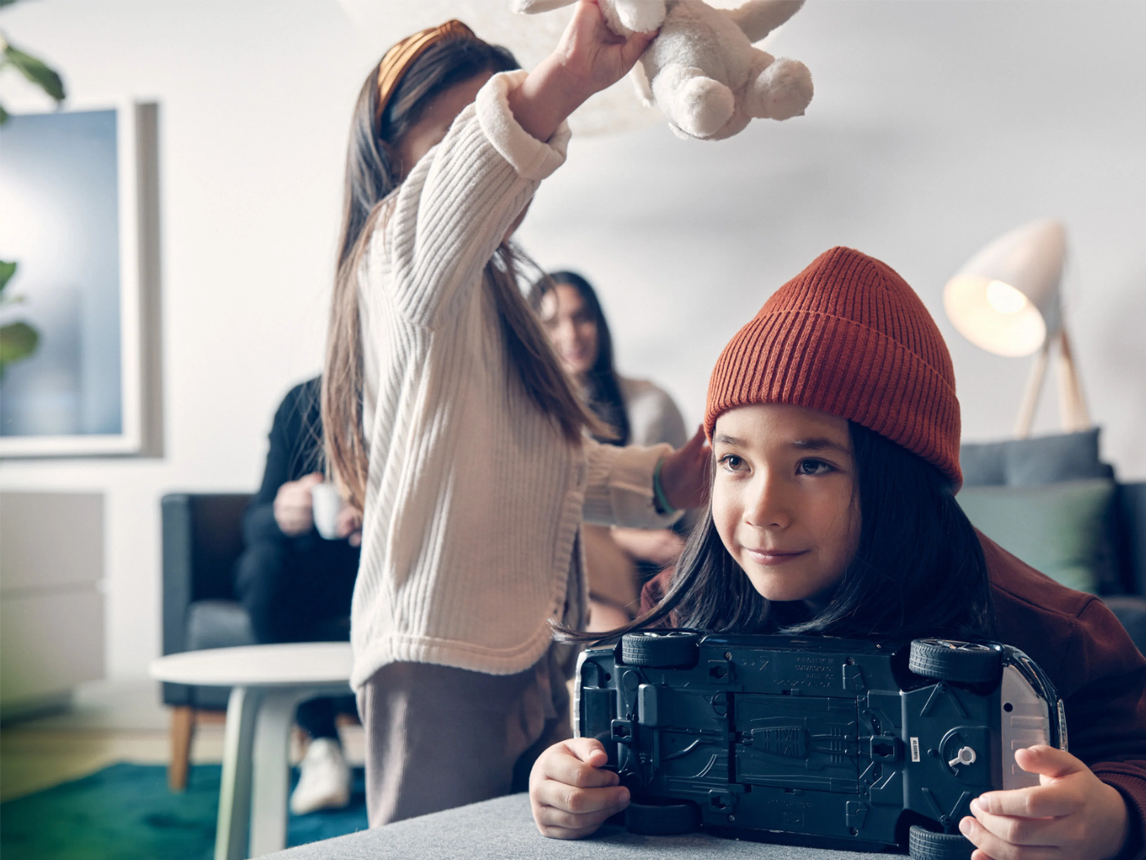 Un enfant portant un bonnet orange tient une voiture miniature Volvo, un autre enfant joue en arrière-plan.