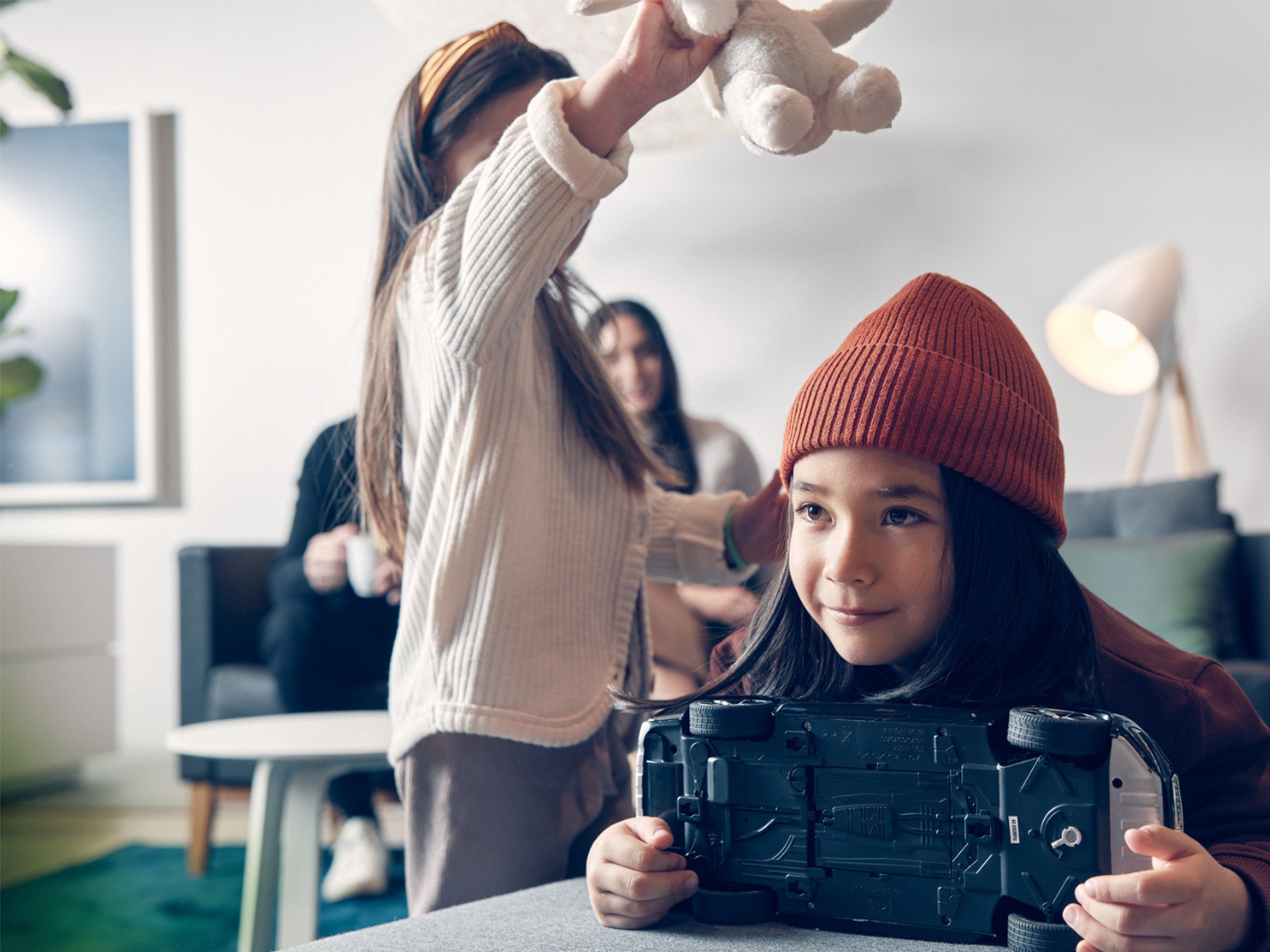 Un enfant portant un bonnet orange tient une voiture miniature Volvo, un autre enfant joue en arrière-plan.