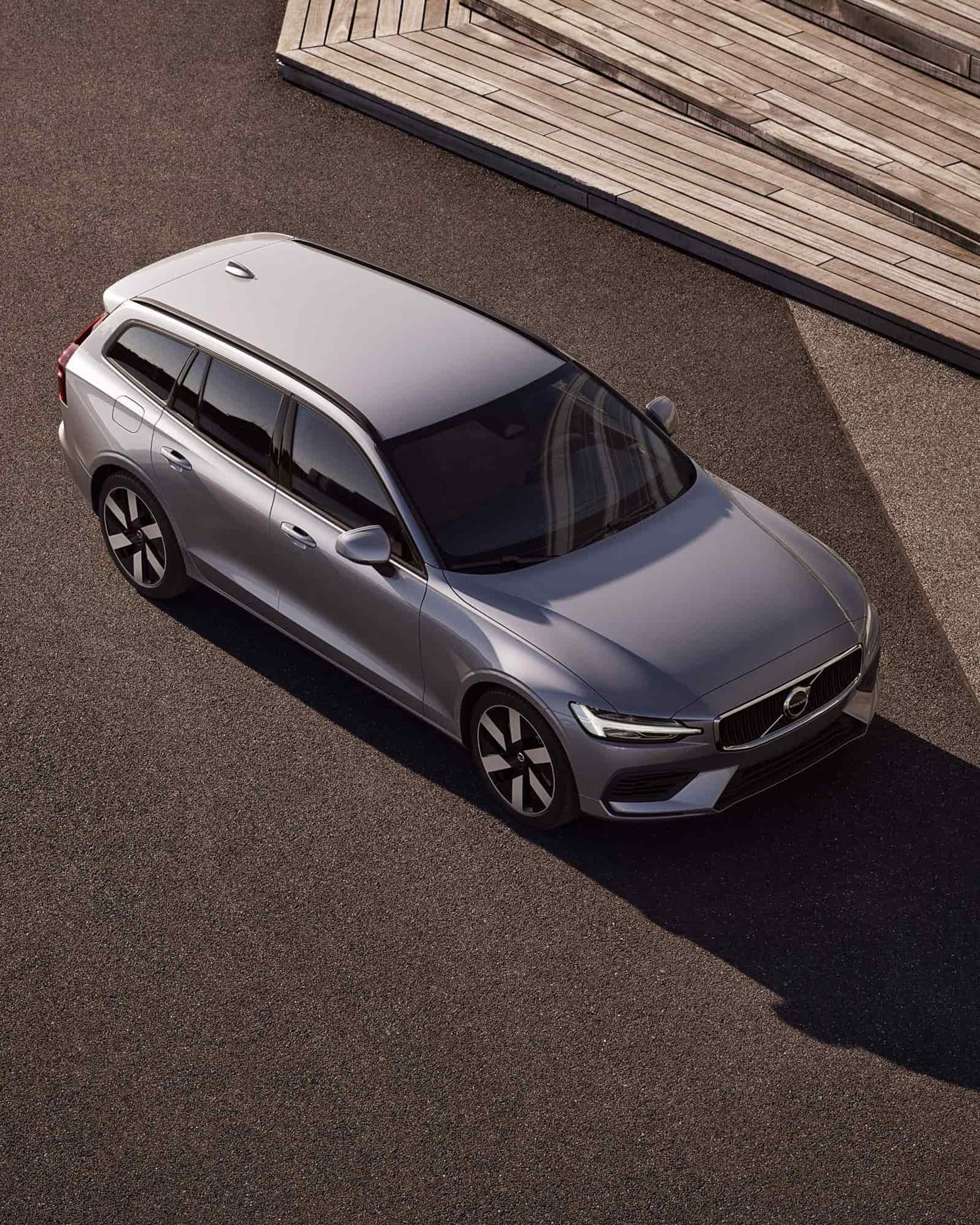 Een grijze Volvo V60 plug-in hybrid in bovenaanzicht die rijdt op een aarden ondergrond met houten trappen aan de zijkant.