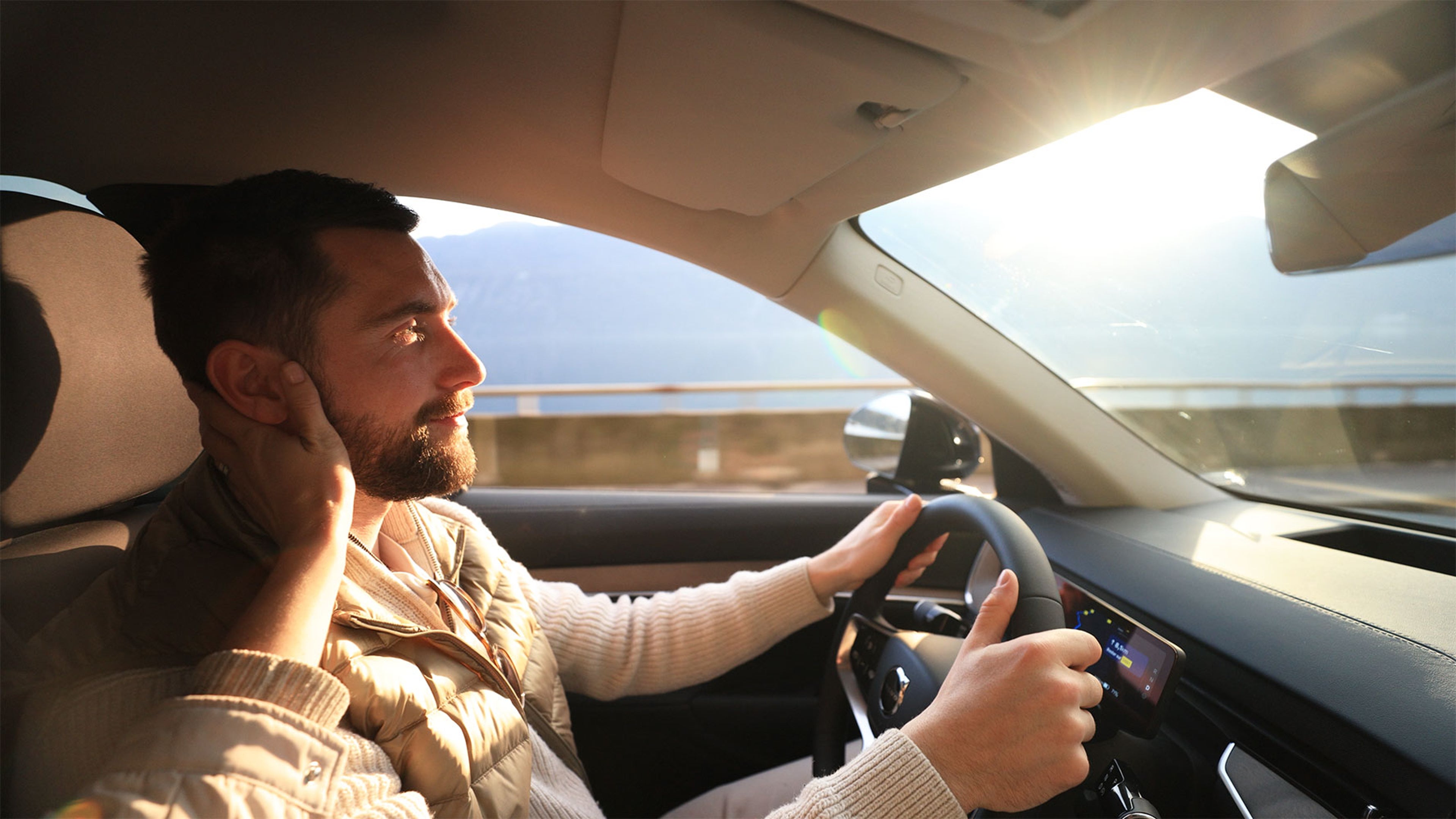 Conducteur concentré, main sur le volant et l’autre sur le visage, en plein jour.