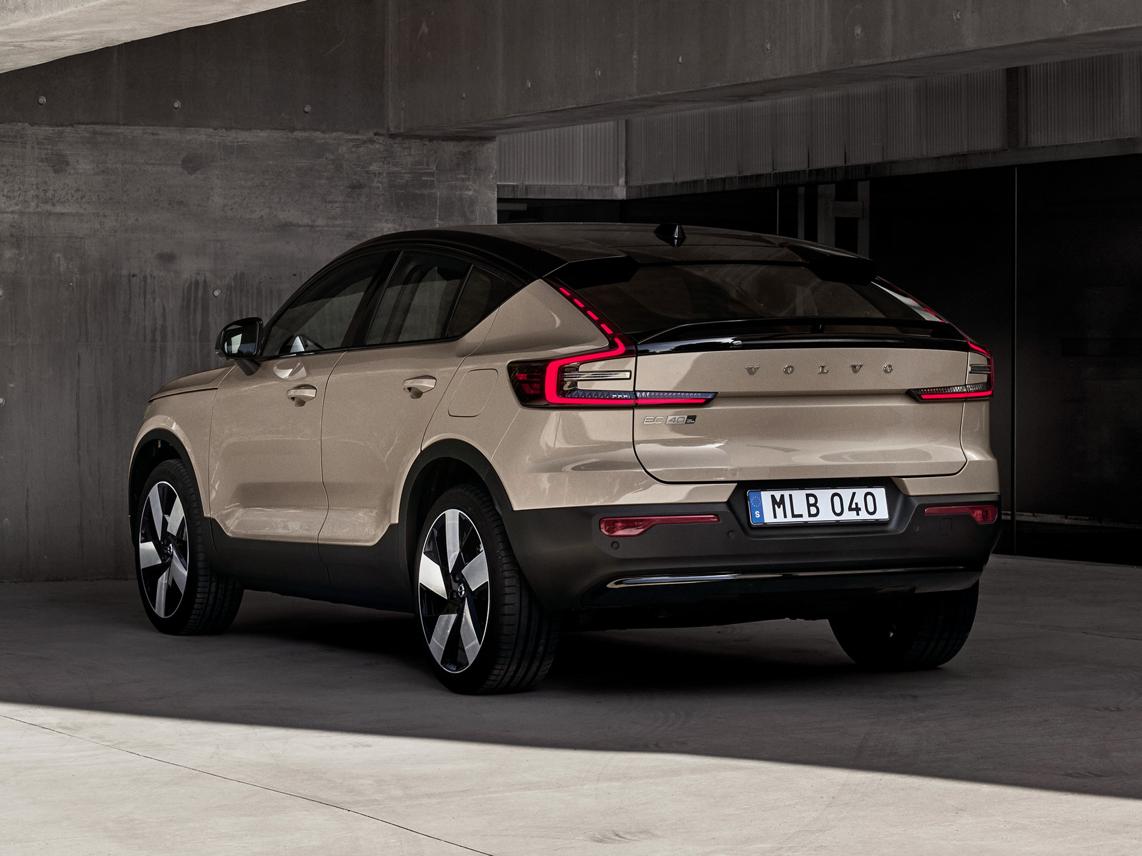Betonisen katoksen alle pysäköity Sand dune -värinen Volvo EC40 täyssähköauto takaviistosta kuvattuna..