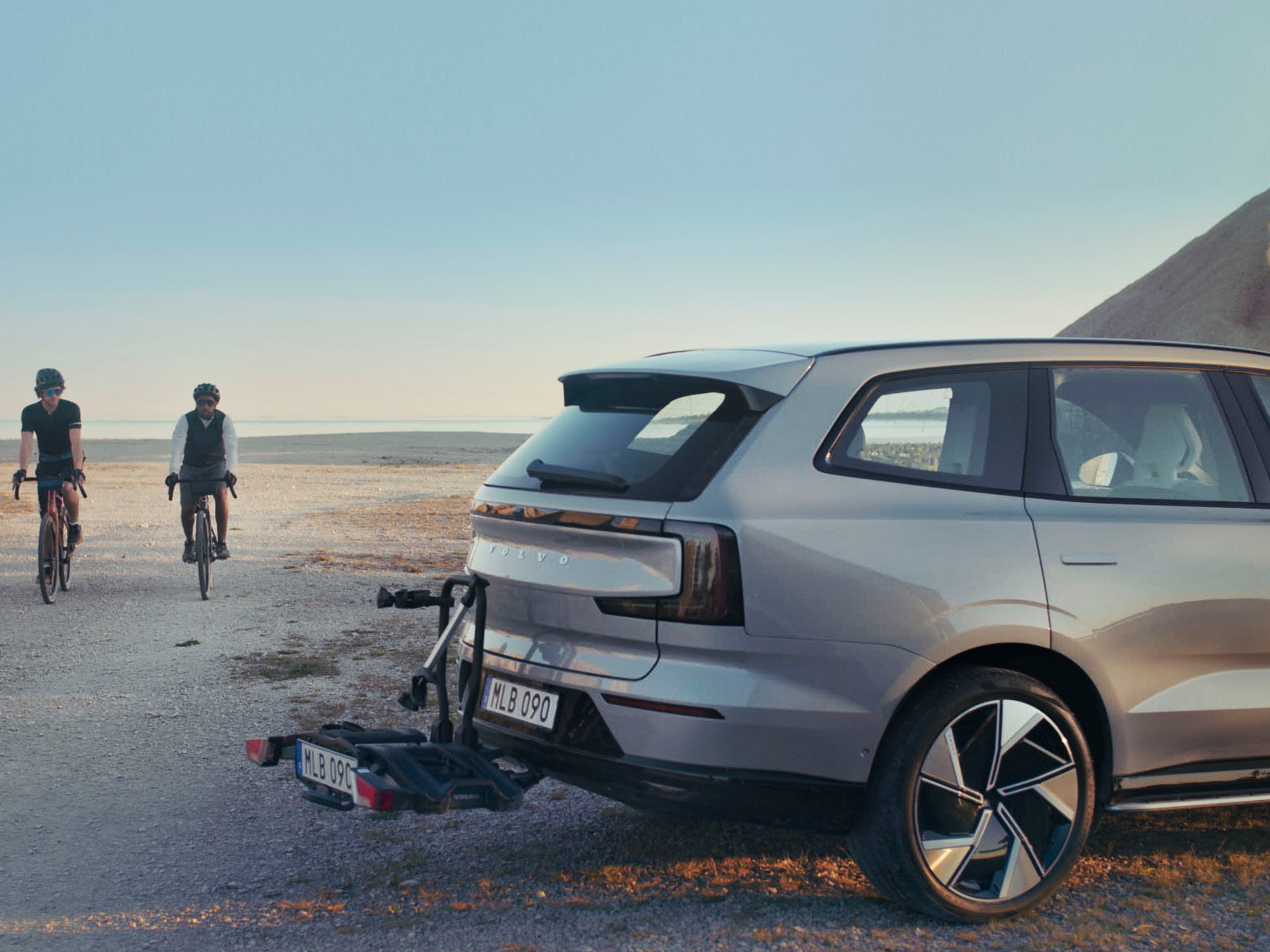 Un Volvo EX90 SUV grande eléctrico con dos ciclistas acercándose.