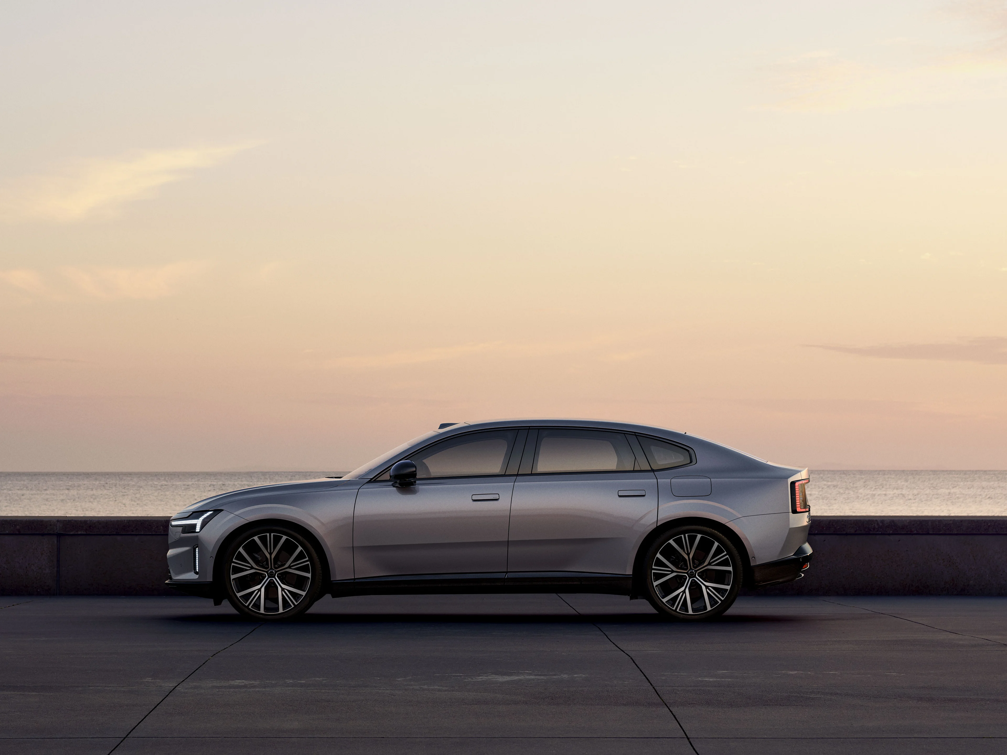 Ein grauer Volvo ES90 Limousine steht auf einer Straße in der Abenddämmerung.