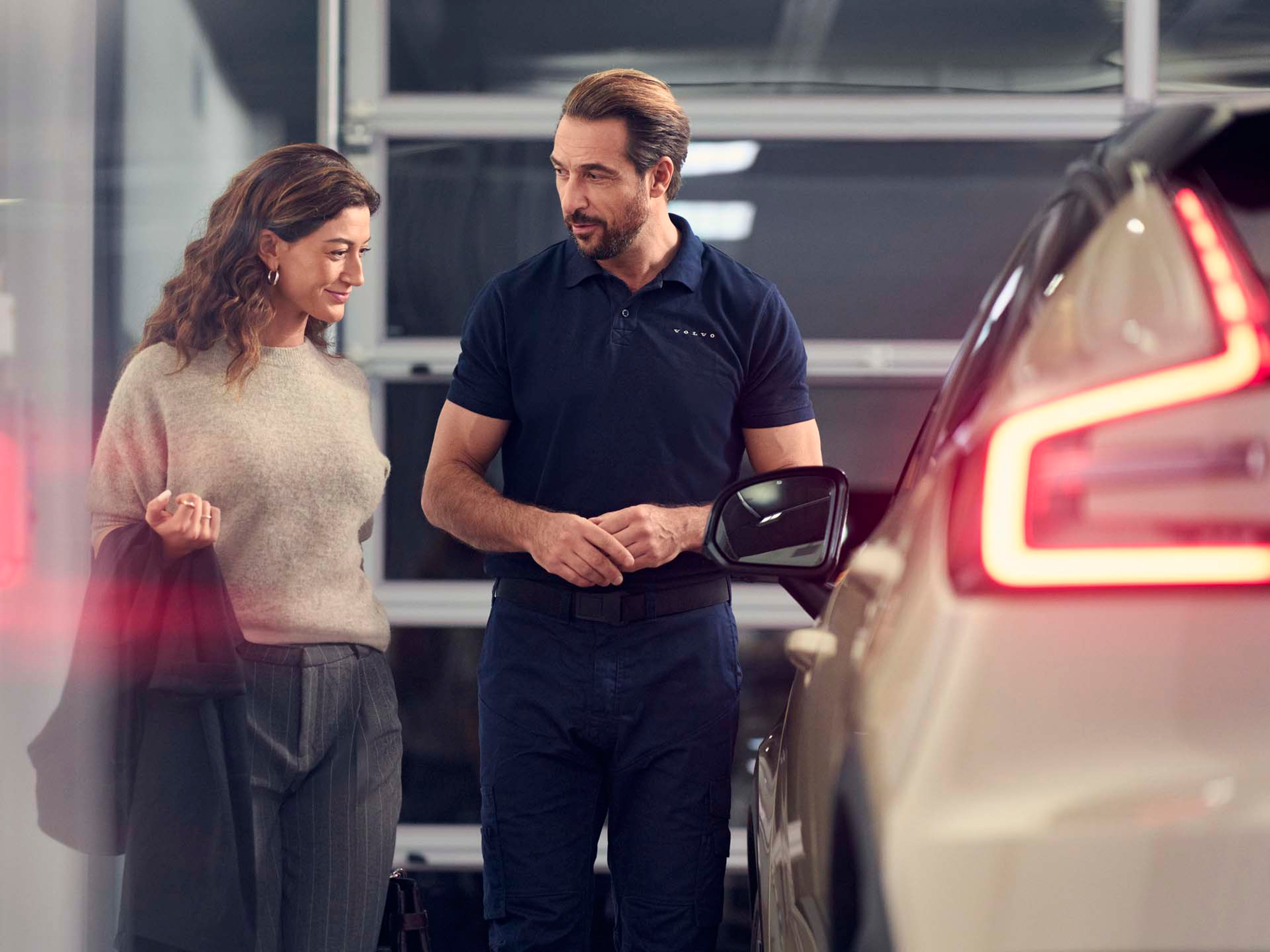 Un especialista de un concesionario Volvo hablando con una cliente entre los vehículos de la concesión.