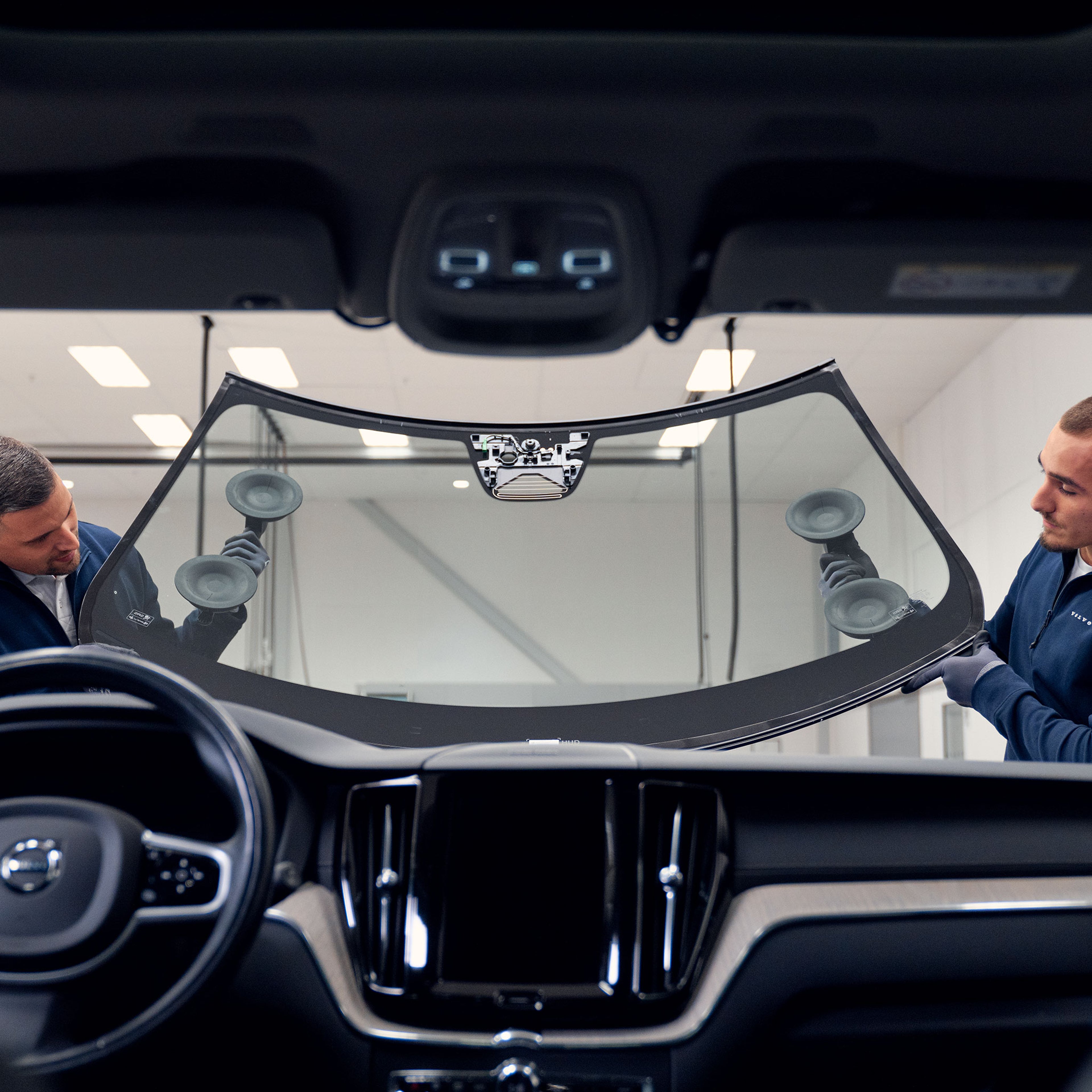 Kaksi Omamekaanikkoa asettaa tuulilasia paikoilleen.