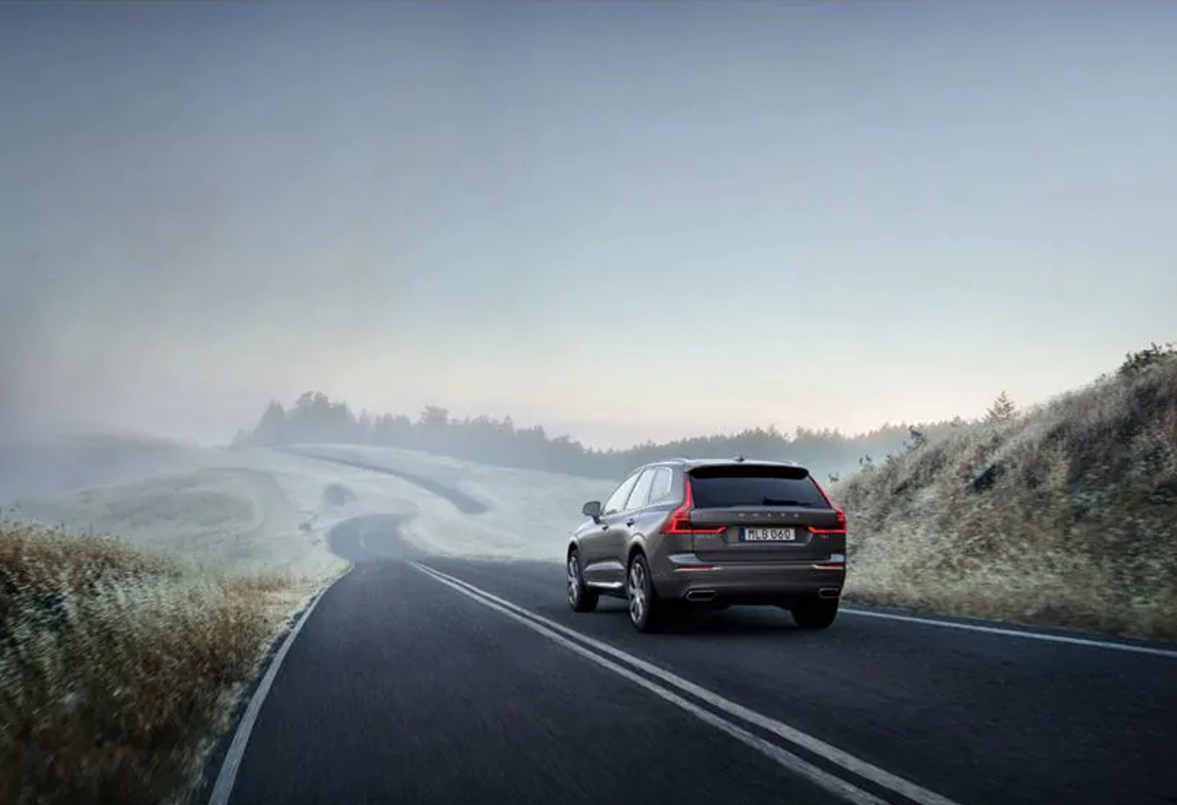Ein dunkelgrauer Volvo XC60 SUV fährt auf einer nebligen Landstraße.