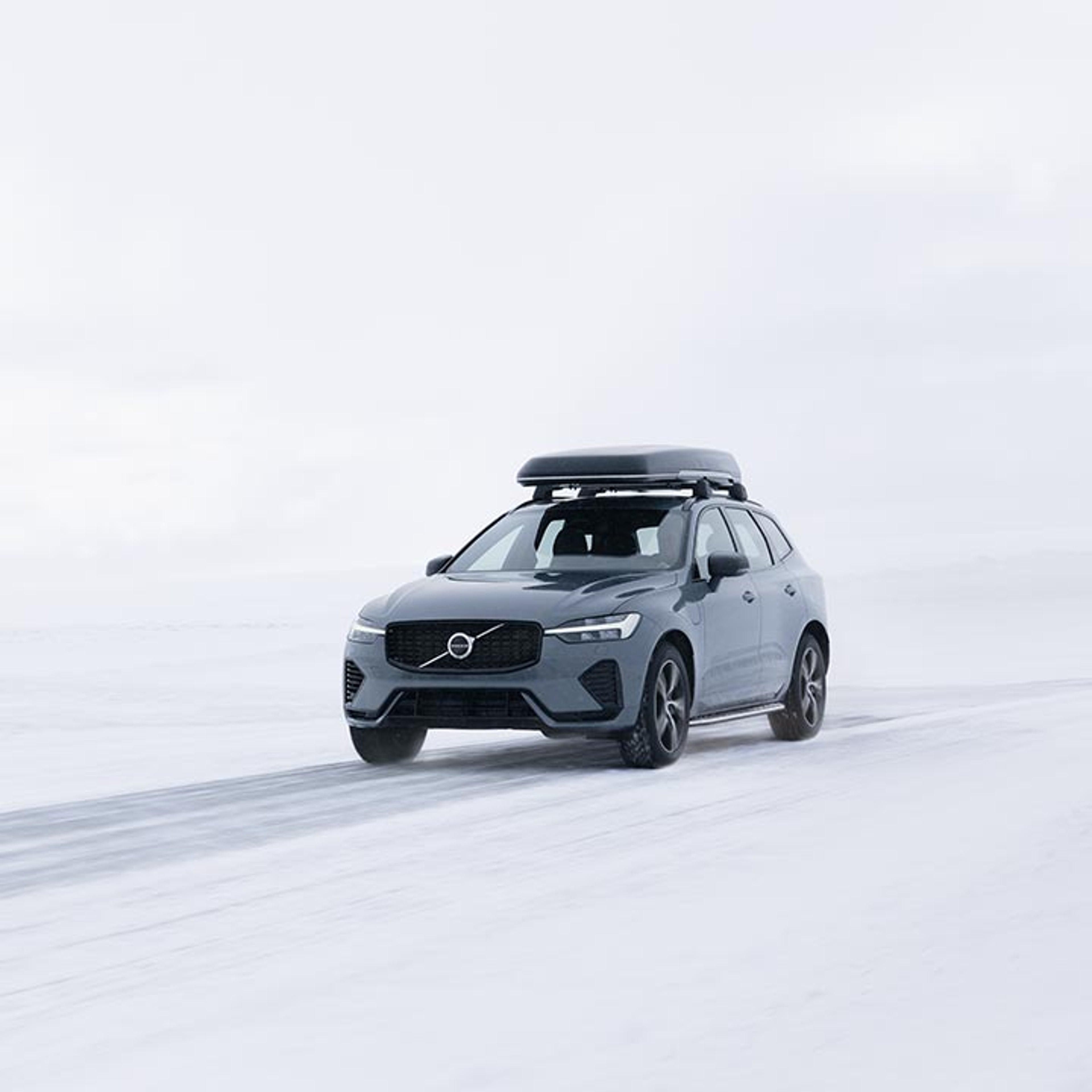 Abbildung eines grauen Volvo XC60 SUV mit Dachbox in einer Winterlandschaft.