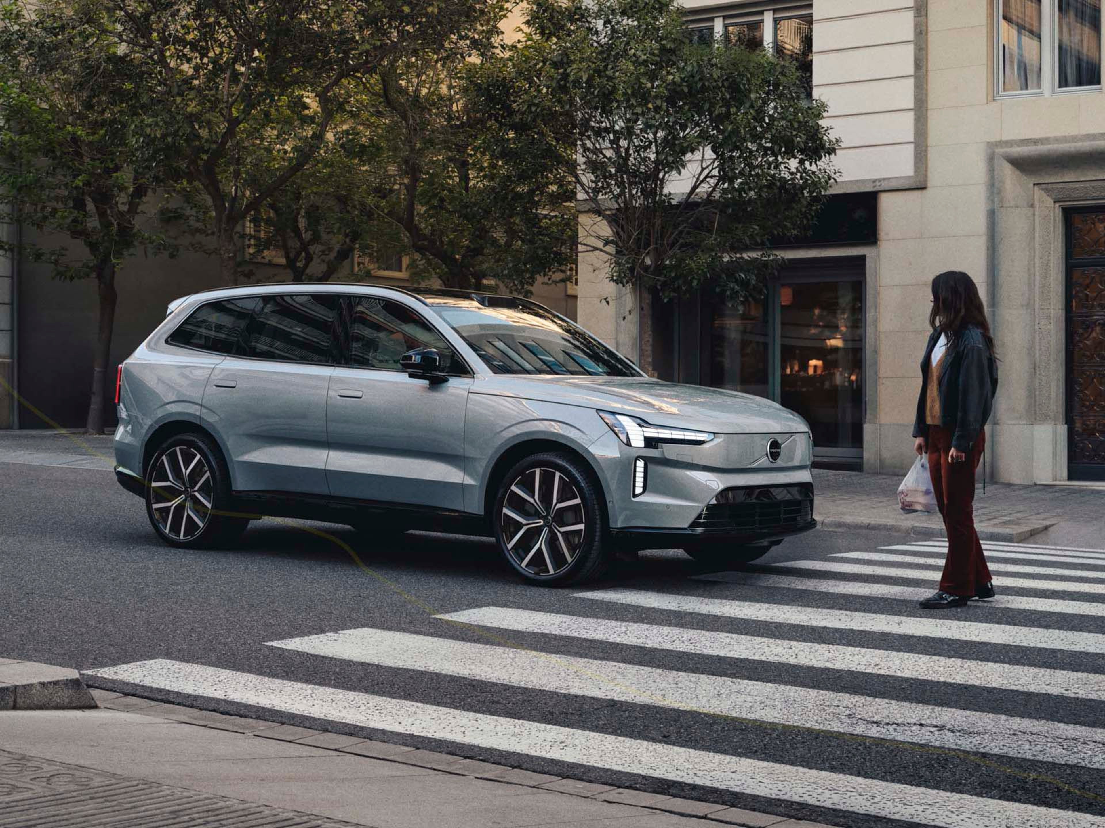 Una mujer cruzando una calle y un Volvo EX90 eléctrico esperando