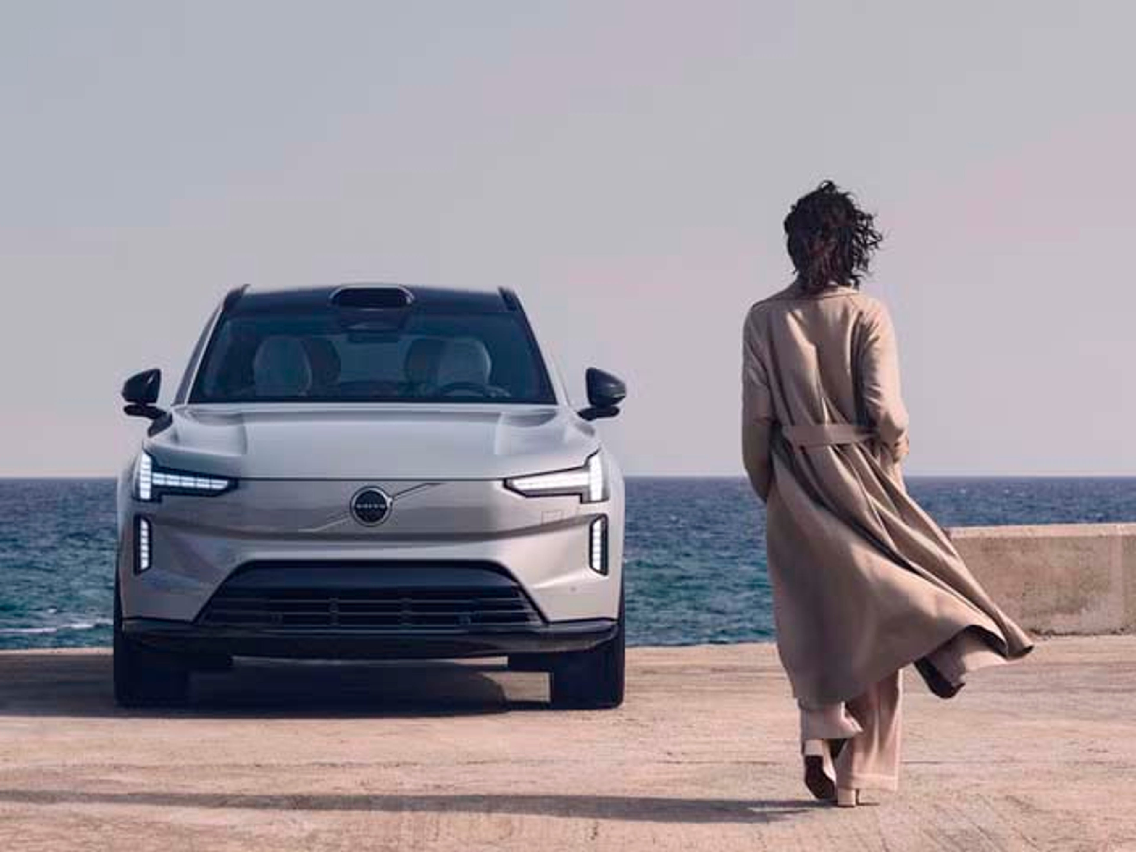 Una mujer caminando hacia su vehículo Volvo junto al mar