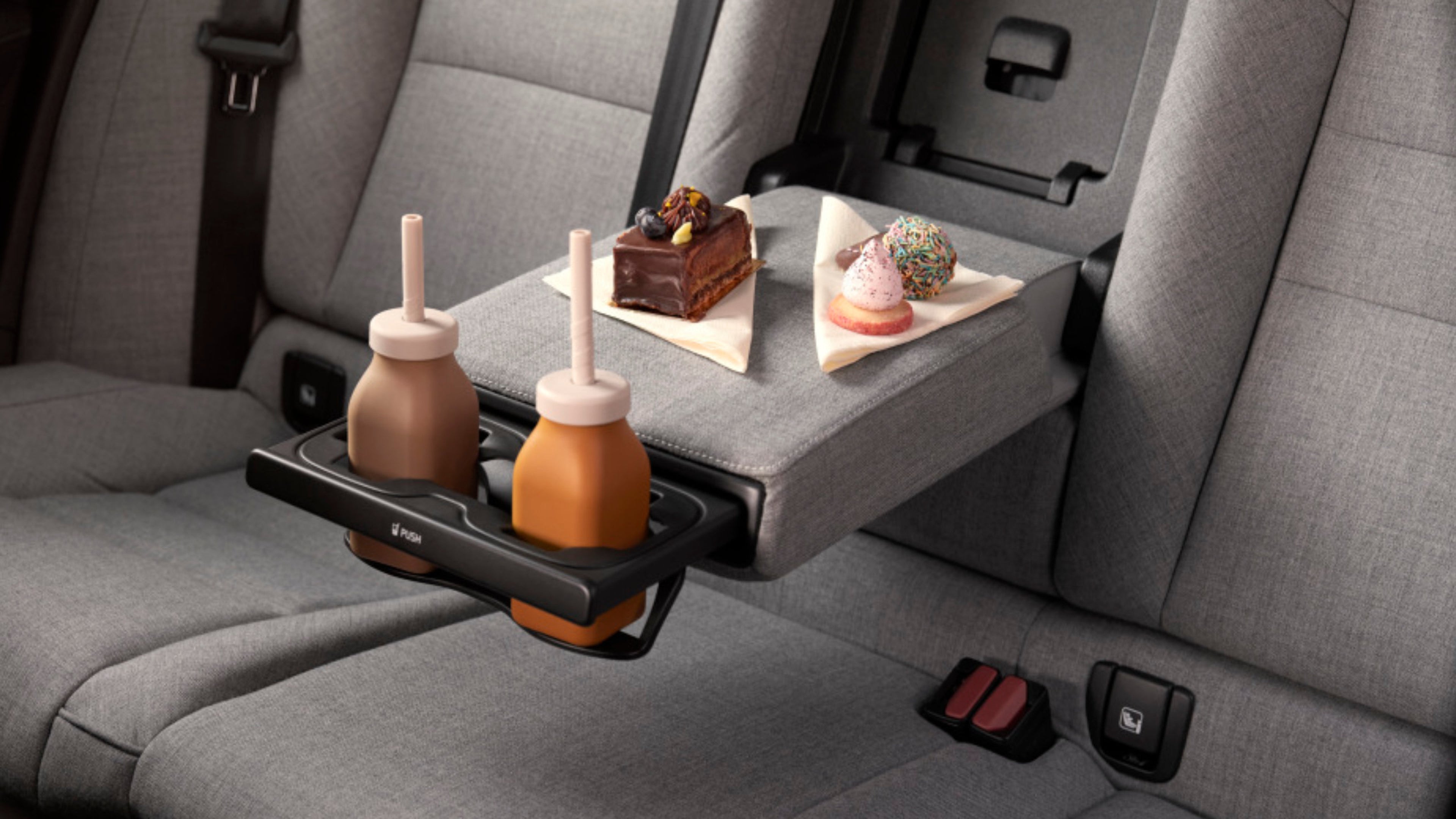 Ein Stück Kuchen sowie zwei Kekse mit Sahne darauf stehen auf der Mittelkonsole zwischen den hinteren Sitzen und zwei Milkshakes stehen in den Getränkehaltern der Mittelkonsole.