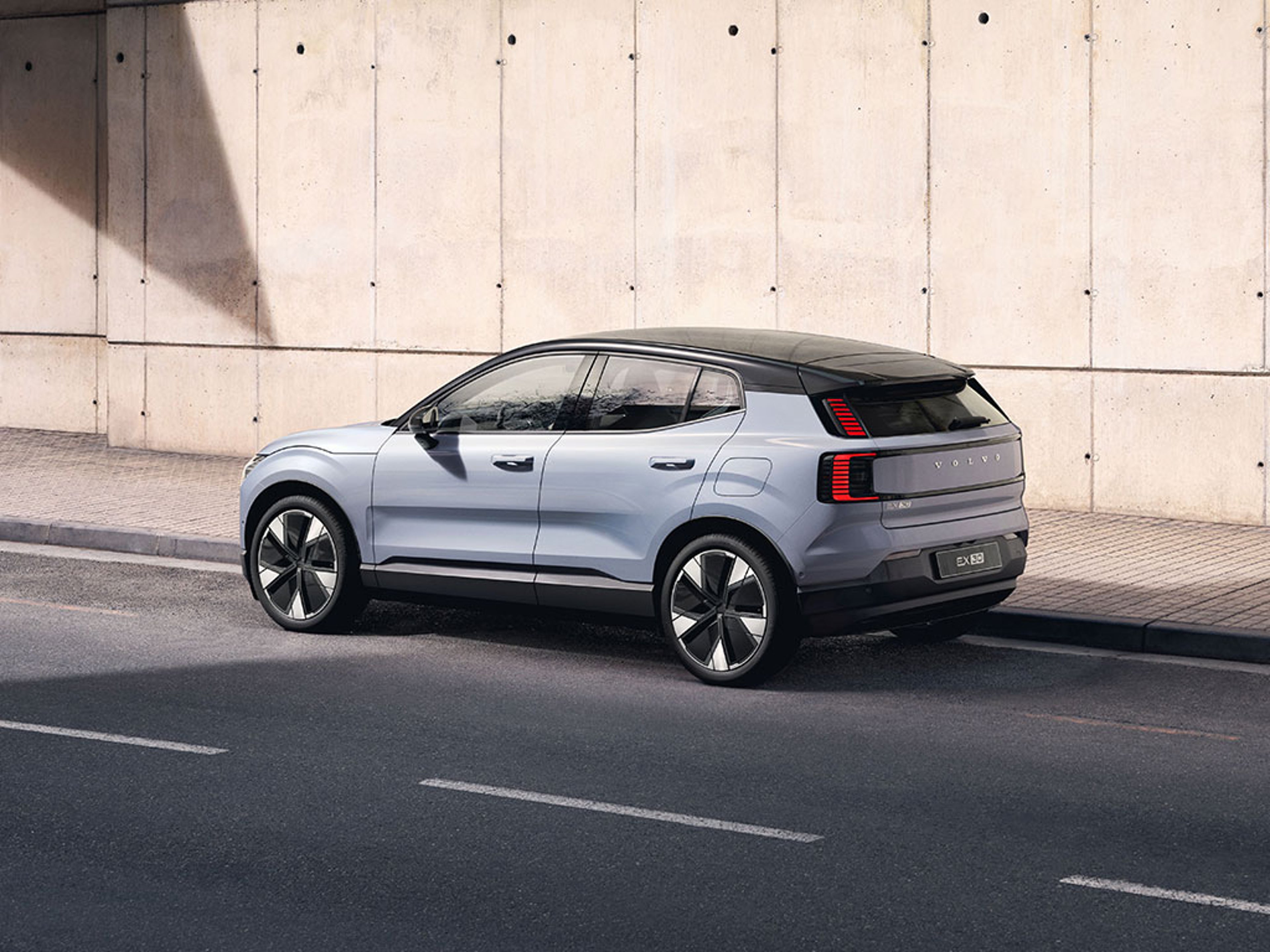 Volvo EX30 argenté garé au bord d’une rue avec un mur en béton en arrière-plan.