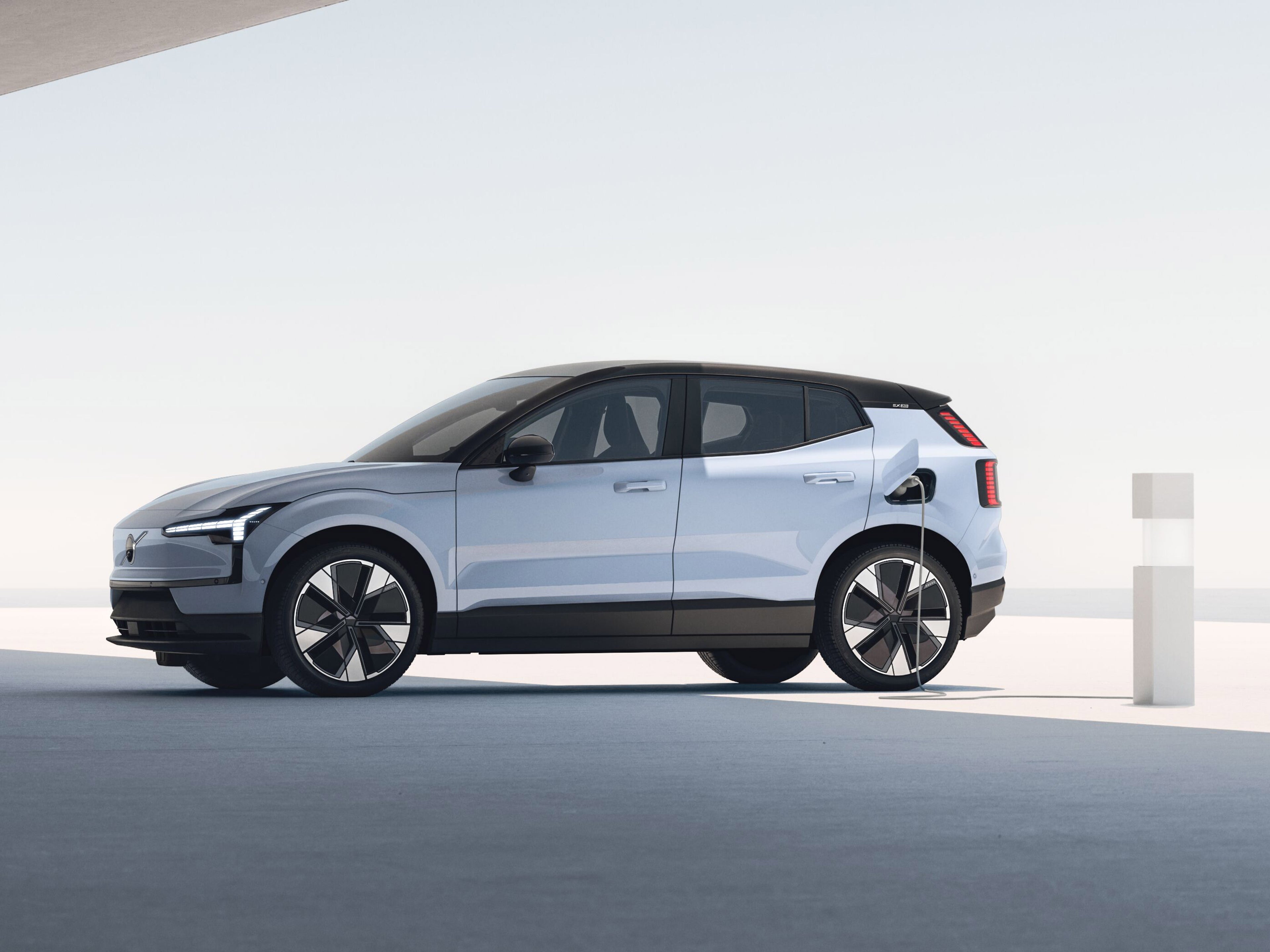 Cloud Blue värinen Volvo EX30 täyssähköauto kytkettynä latauspisteeseen.
