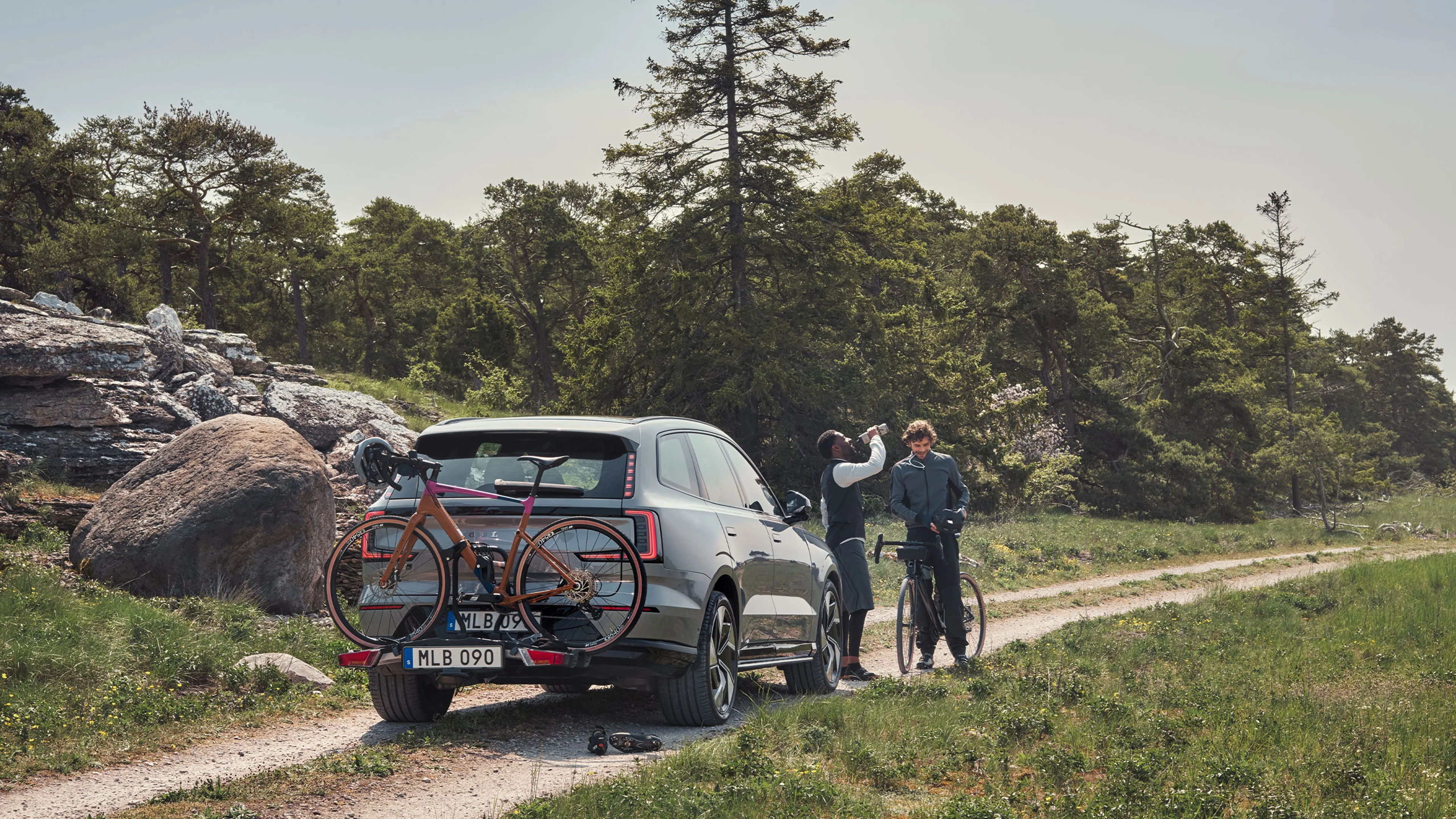 Zwei Männer stehen vor einem silbernen Volvo EX90 mit Fahrradträger und montiertem Dirt-Bike.