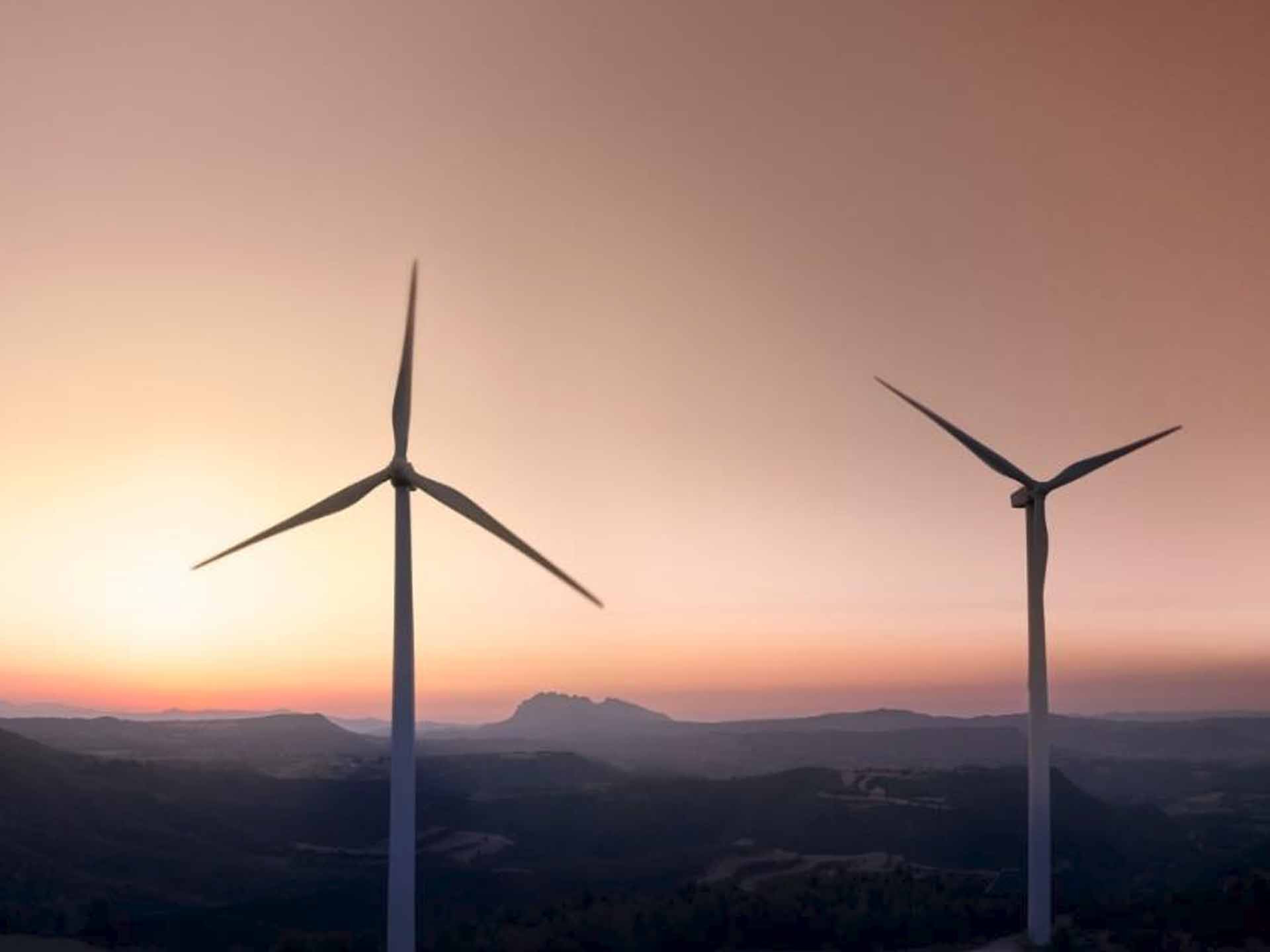 Zwei Windräder stehen im untergehenden Sonnenschein vor einer Wüstenlandschaft.